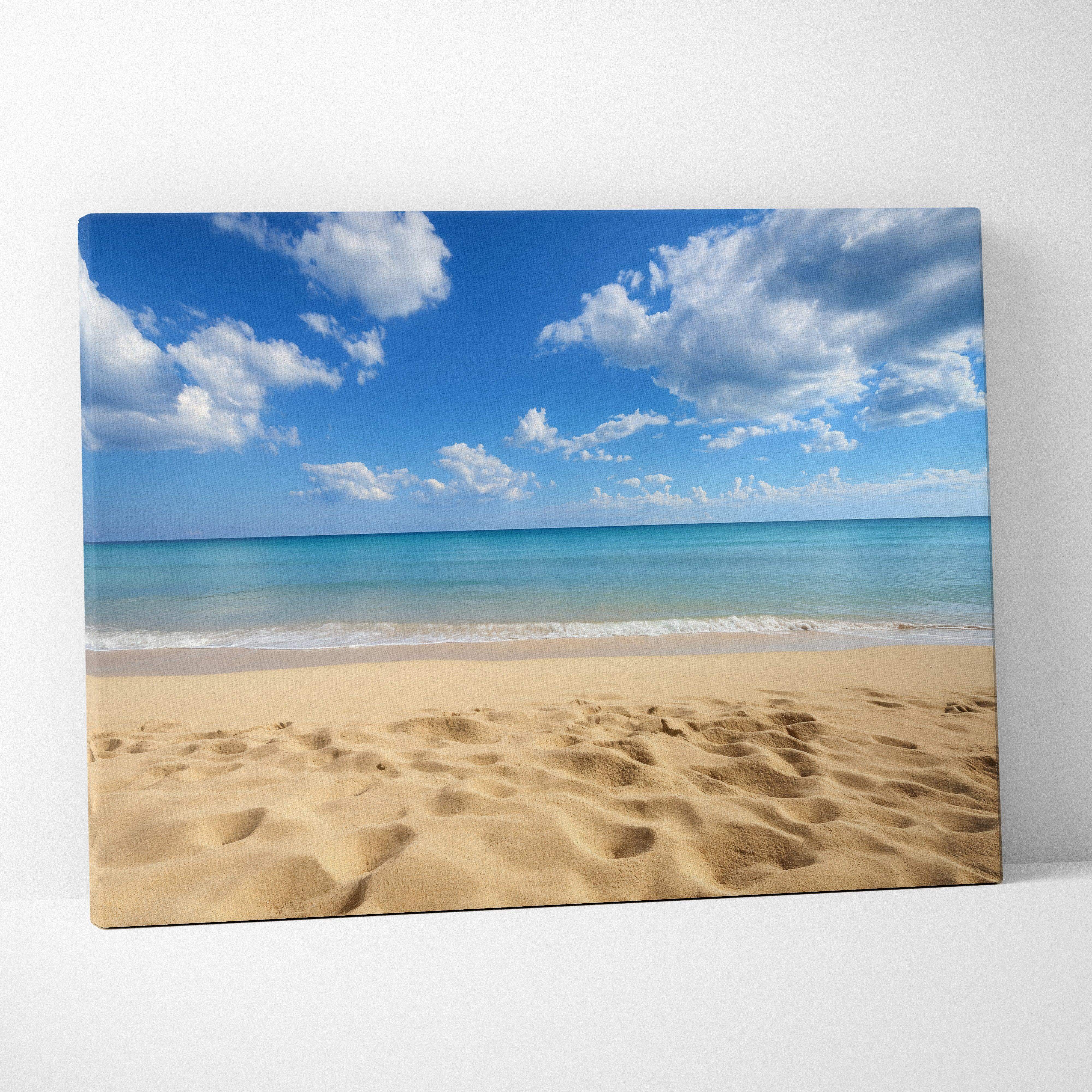 Coastal seascape canvas wall art featuring a turquoise ocean, golden sand with footprints, and bright blue sky with white clouds