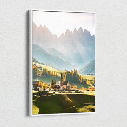 Vertical canvas wall art featuring a sunlit mountain village with sharp peaks and warm golden tones.