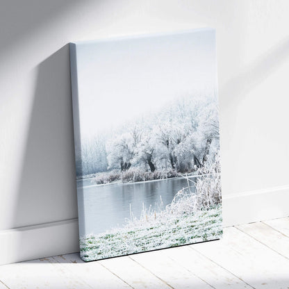 Canvas wall art depicting a serene winter landscape with snow-covered trees by a calm river under a pale sky.