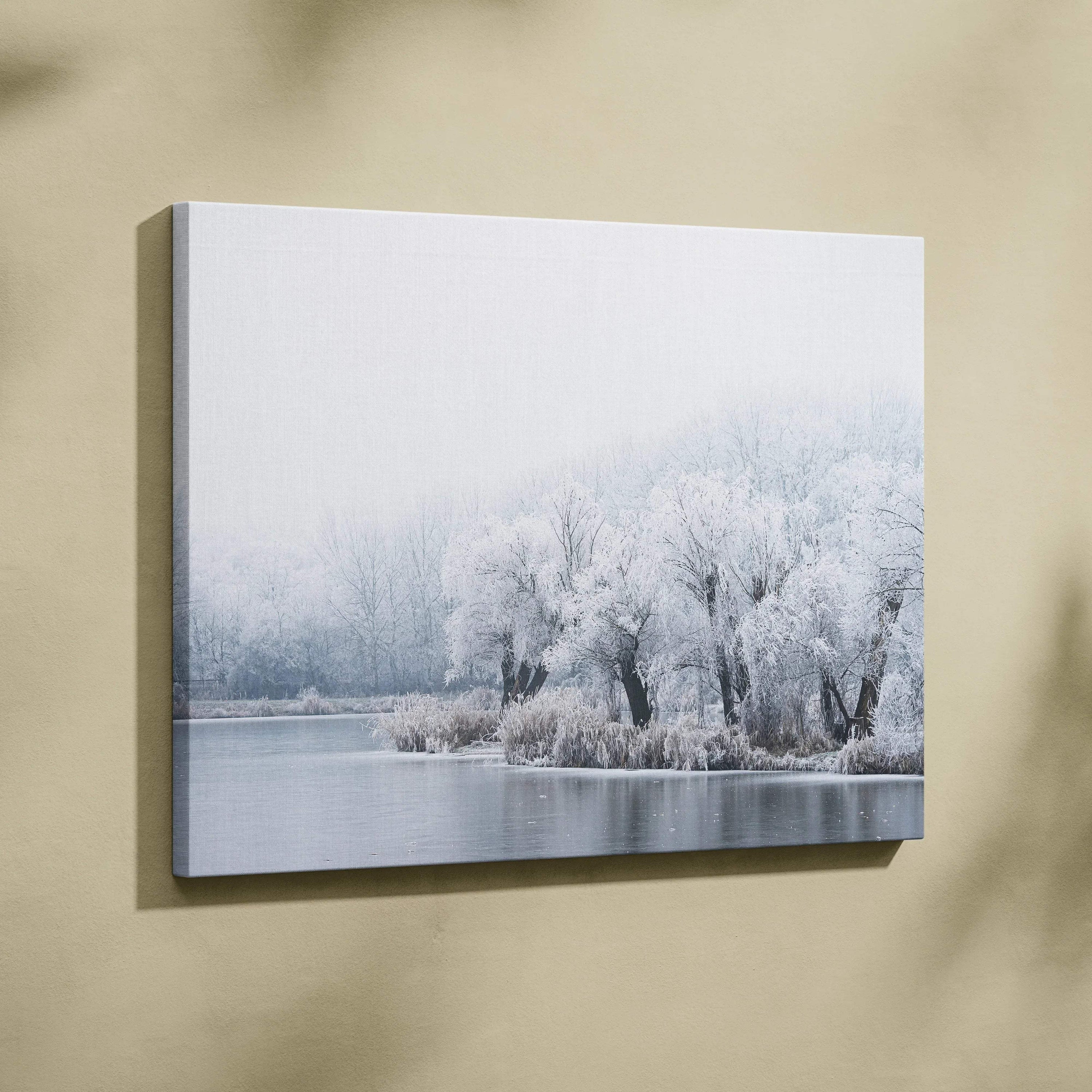 Canvas wall art featuring a serene winter landscape of snow-covered trees by a calm frozen lake.