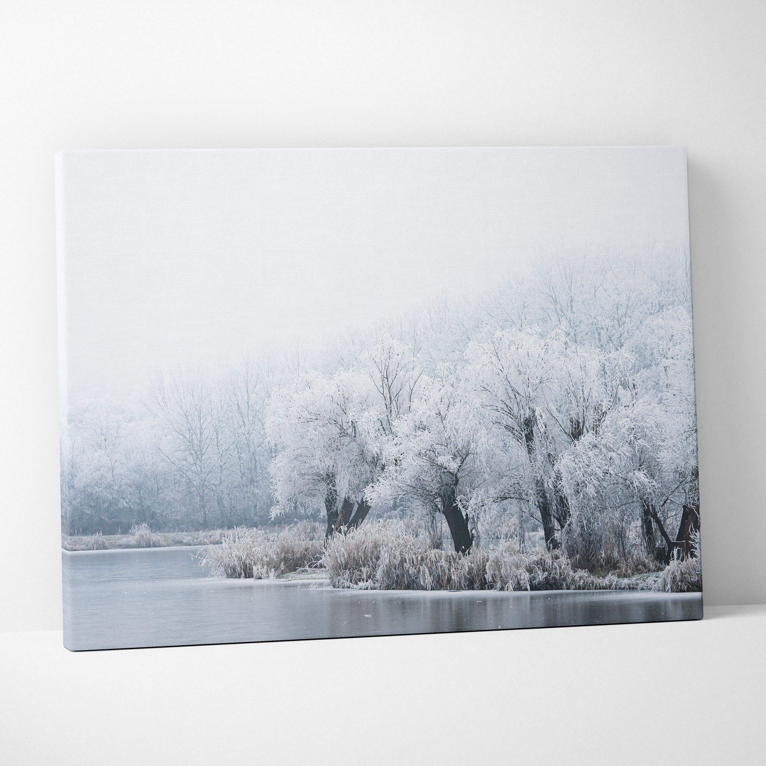 Canvas wall art depicting snow-covered trees with frosty branches by a calm, icy lake under a pale, misty sky.