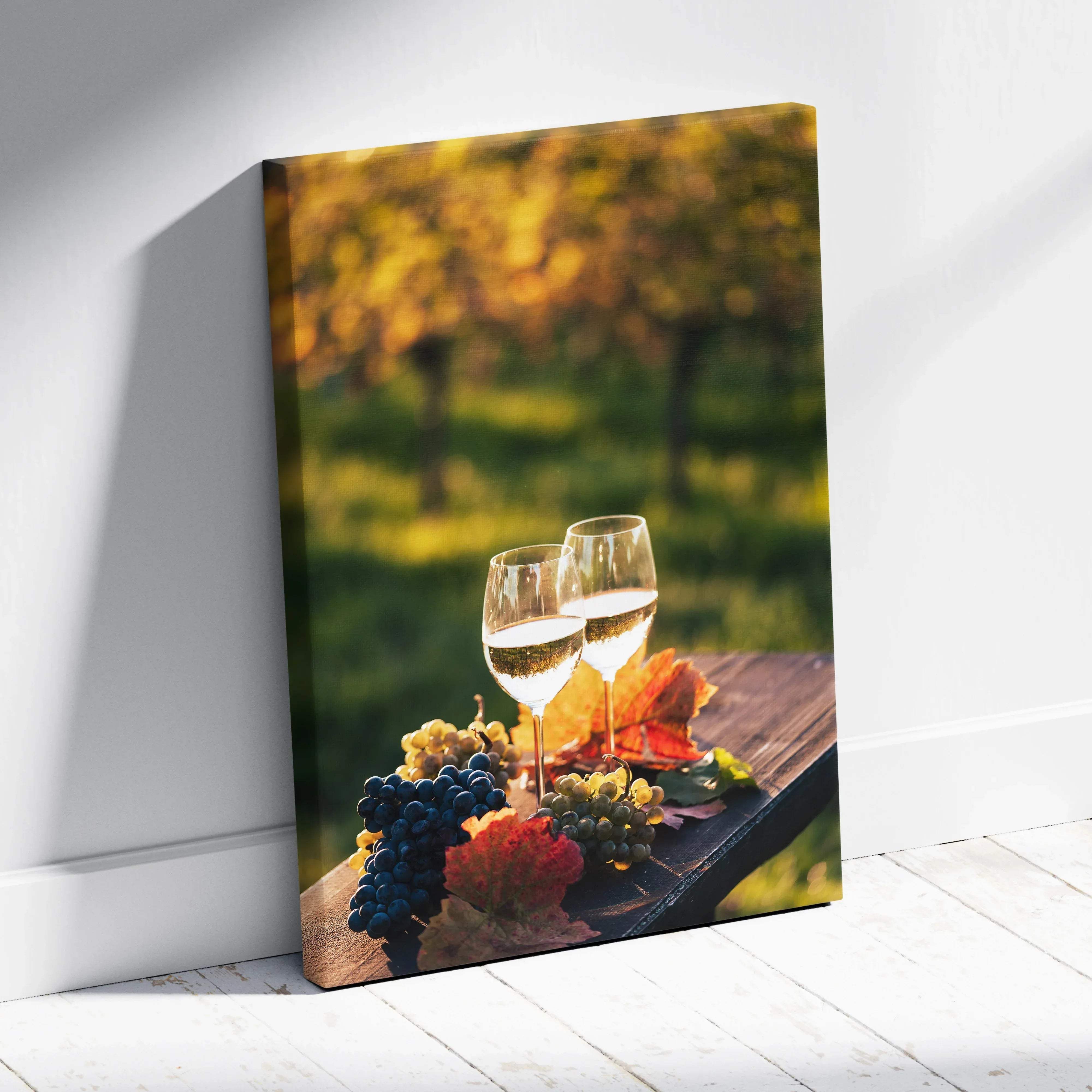 Canvas print of two glasses of white wine and colorful grapes on wooden surface with autumn vineyard background