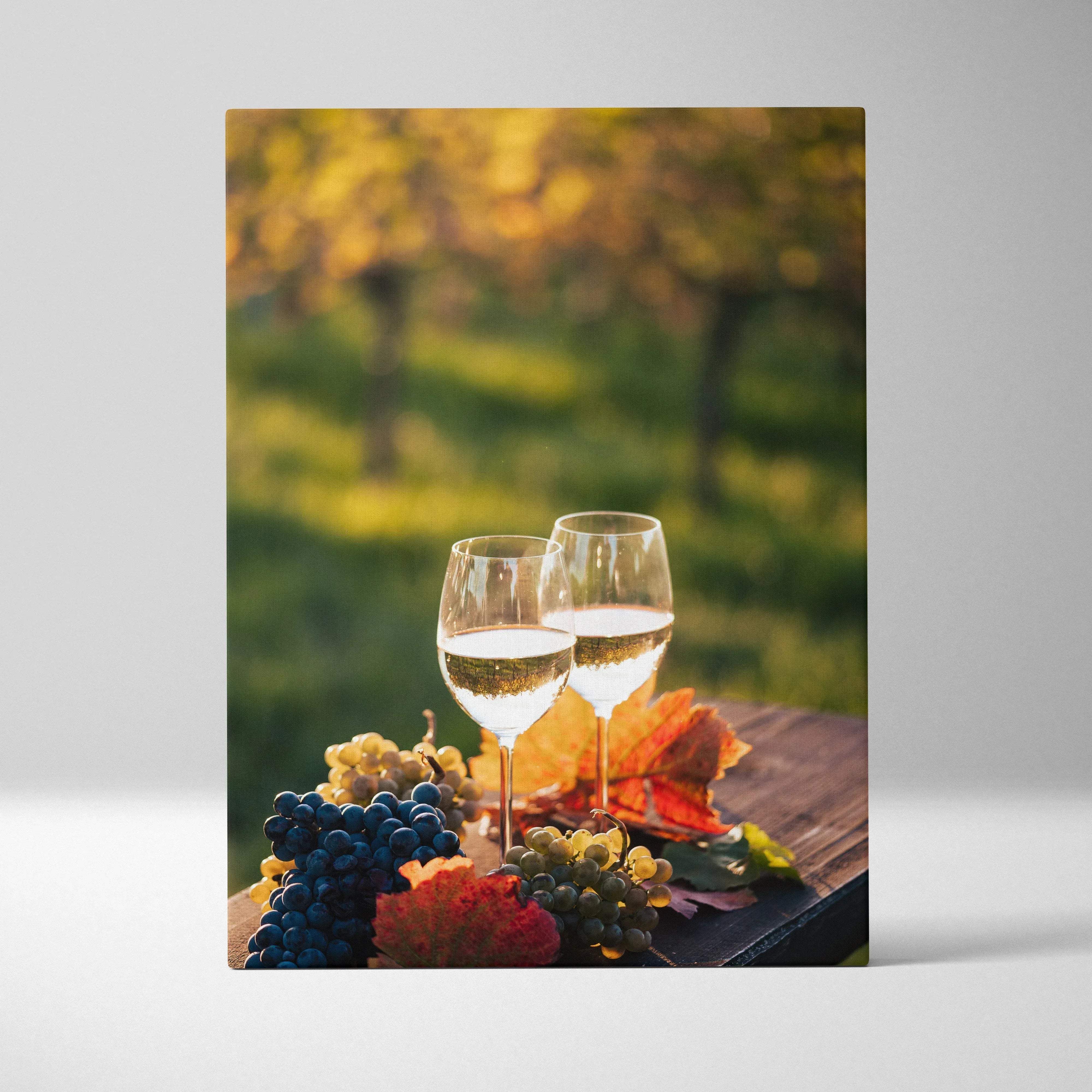 Two elegant clear wine glasses filled with golden white wine beside purple and green grapes on rustic wooden surface