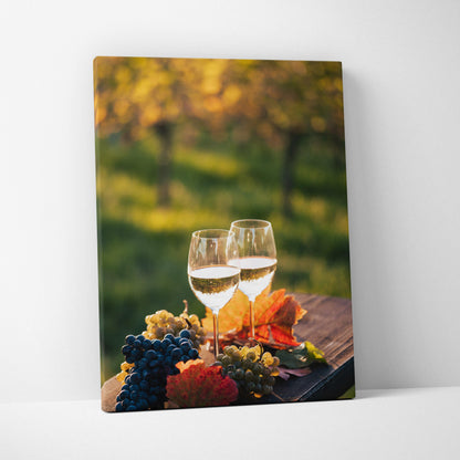 Canvas wall art with two wine glasses, bunches of grapes, and colorful autumn leaves on a wooden table outdoors.