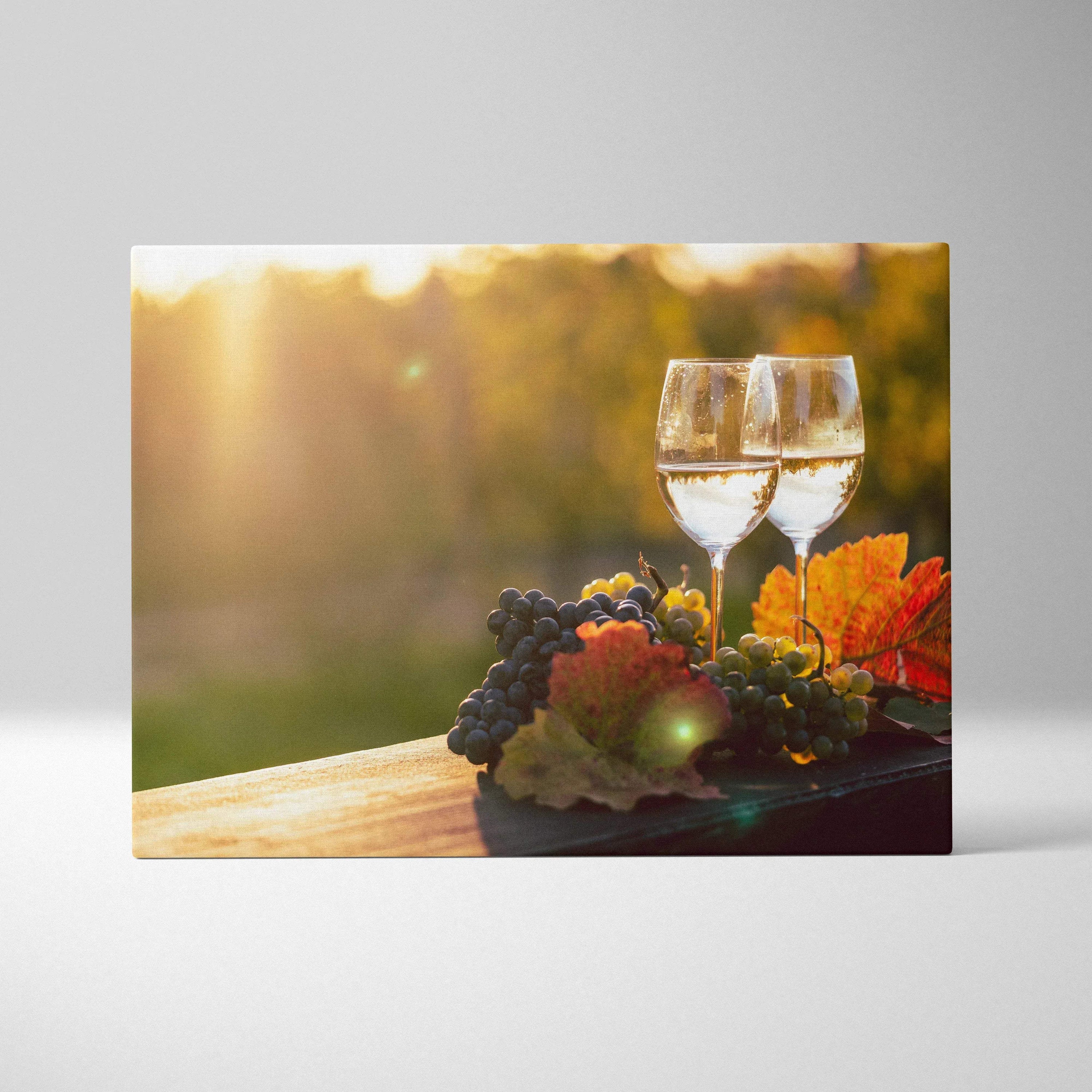 Canvas wall art featuring two wine glasses with white wine, grapes, and autumn leaves on a wooden surface with a soft golden