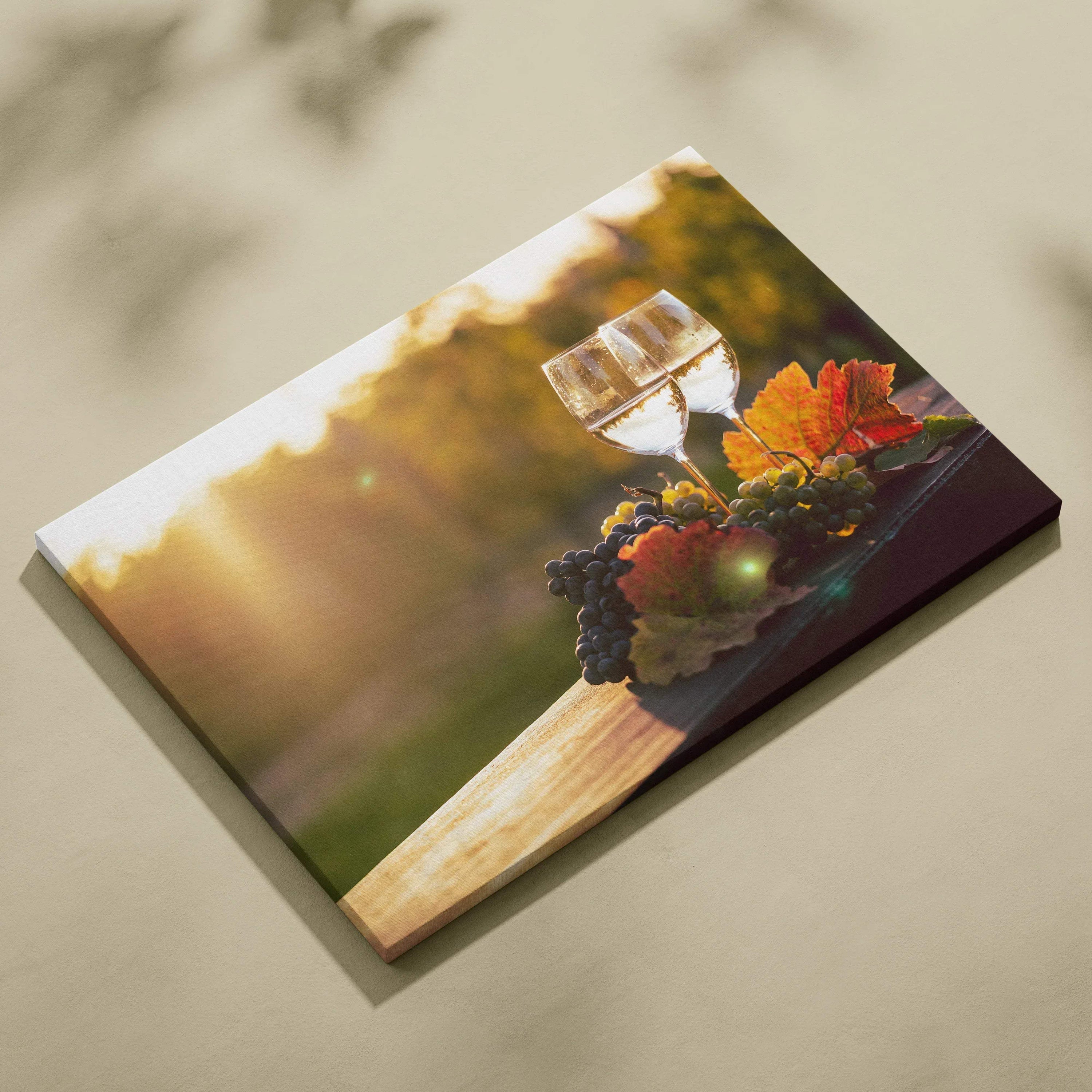 Canvas wall art depicting a glass of white wine with grapes and autumn leaves on a wooden table at sunset.