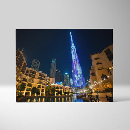 Canvas wall art featuring a nighttime cityscape with a tall, illuminated skyscraper and surrounding buildings reflecting on.