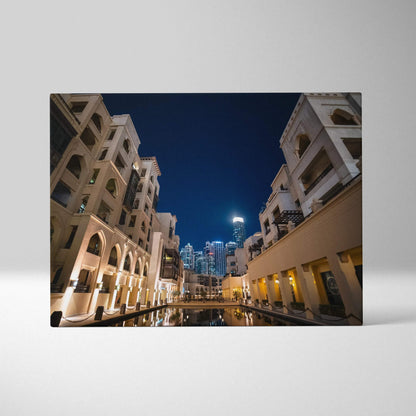Canvas art featuring modern architectural buildings at night with warm lighting and a reflective water surface under a deep.