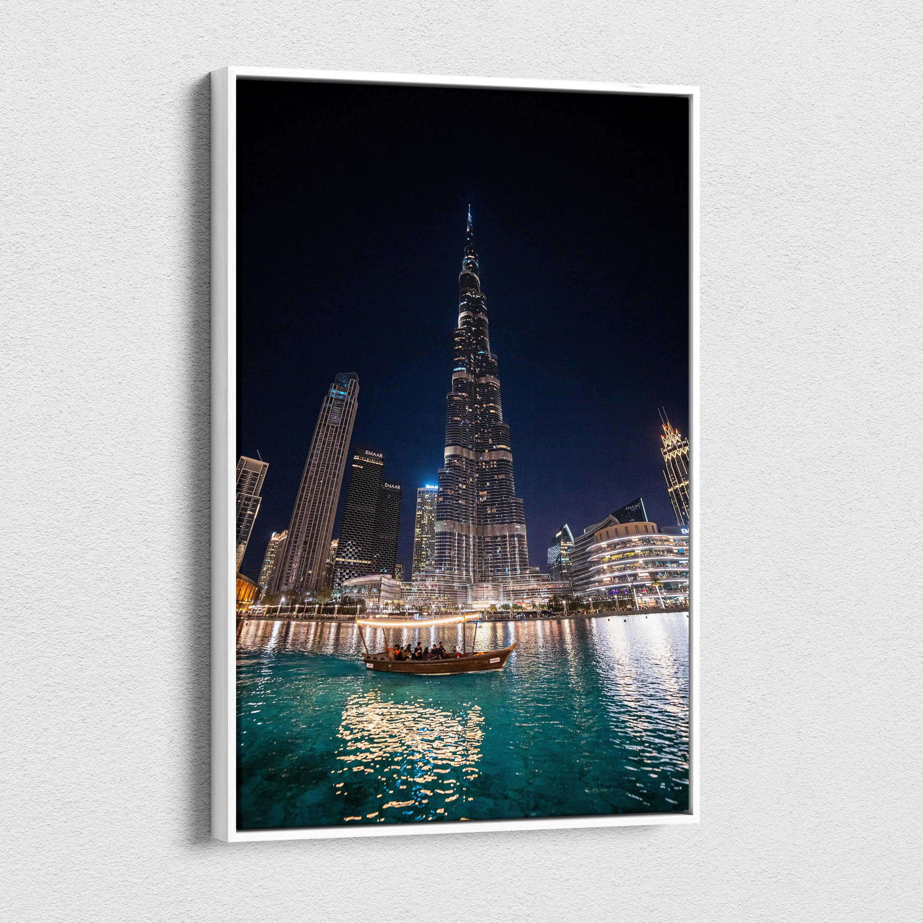 Nighttime cityscape canvas art featuring illuminated skyscrapers, including a tall pointed tower, over turquoise water with.