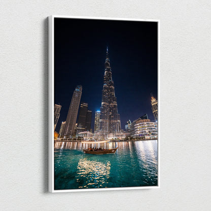 Nighttime cityscape canvas art featuring illuminated skyscrapers, including a tall pointed tower, over turquoise water with.