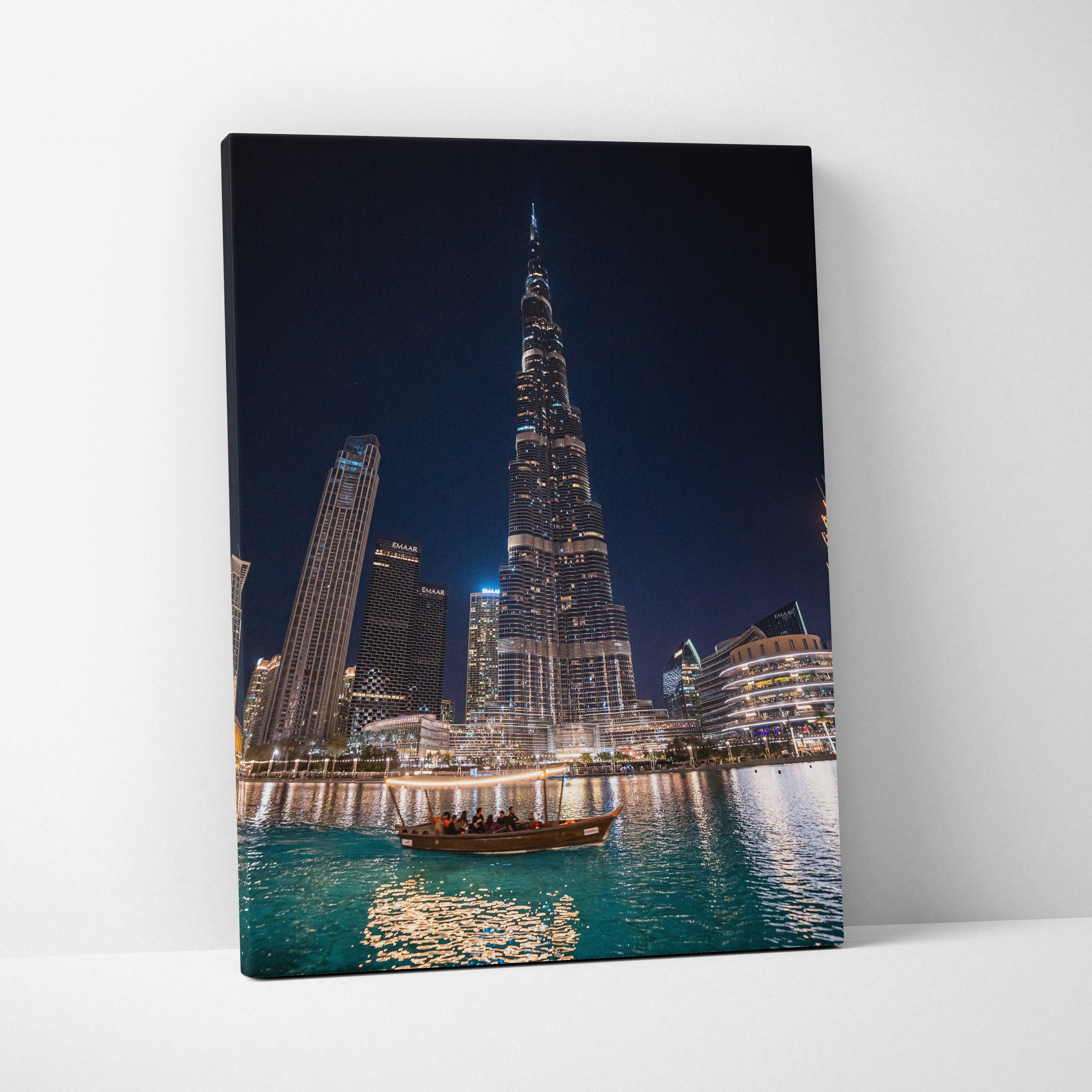 Tall modern skyscraper with illuminated windows and reflections on water, printed on rectangular canvas wall art.