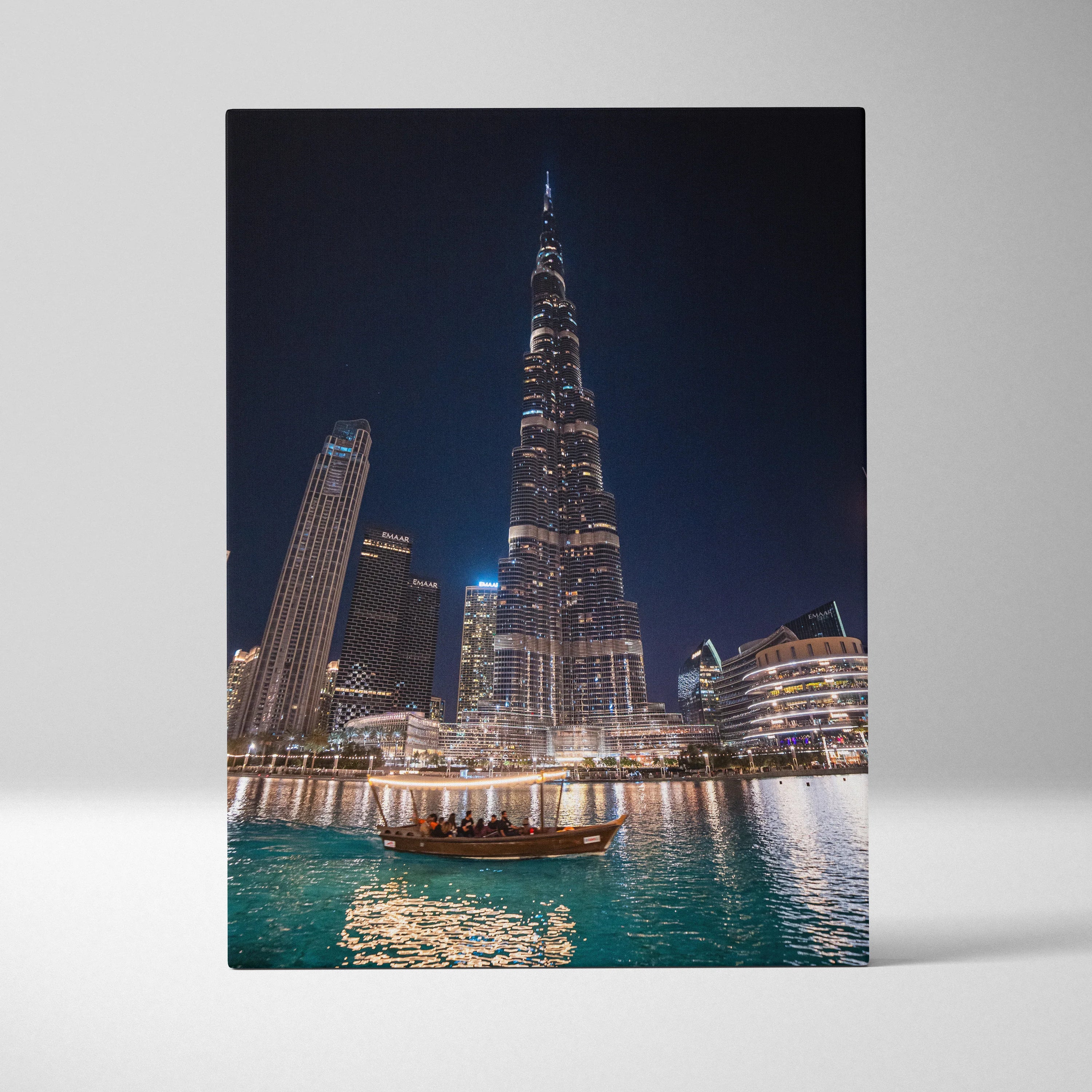 Vertical canvas wall art featuring illuminated modern skyscrapers at night with reflective water below.