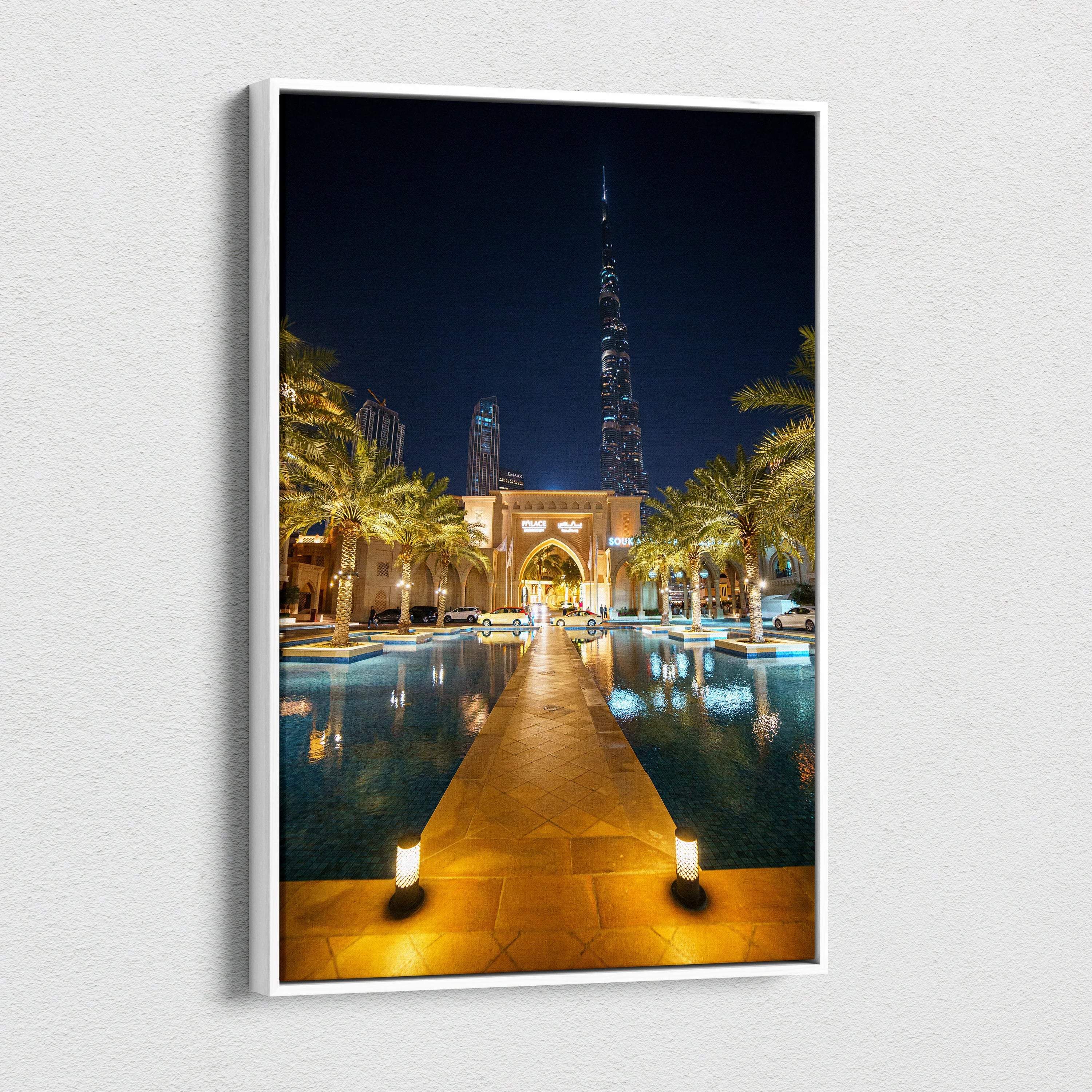 Vertical canvas wall art featuring illuminated urban architecture with a nighttime cityscape and reflective water pool.