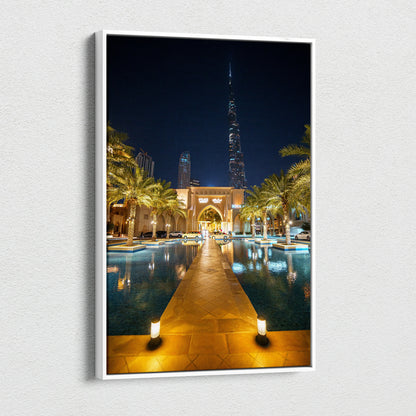 Vertical canvas wall art featuring illuminated urban architecture with a nighttime cityscape and reflective water pool.