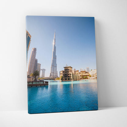 Canvas wall art featuring a tall modern skyscraper and surrounding buildings reflected in blue water under a clear sky.