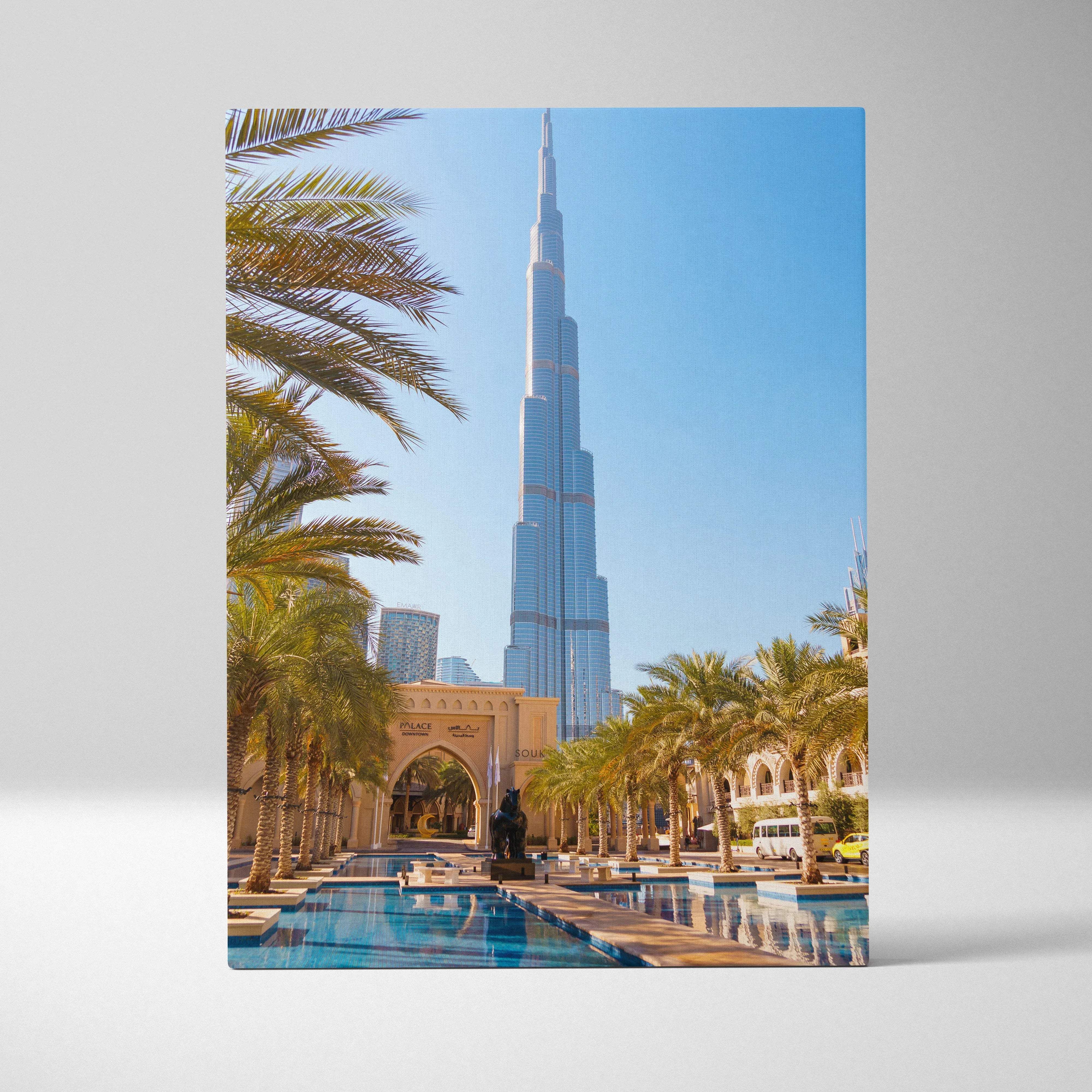 A rectangular canvas print featuring the burj khalifa with silver-blue glass, palm trees, and a bright blue sky