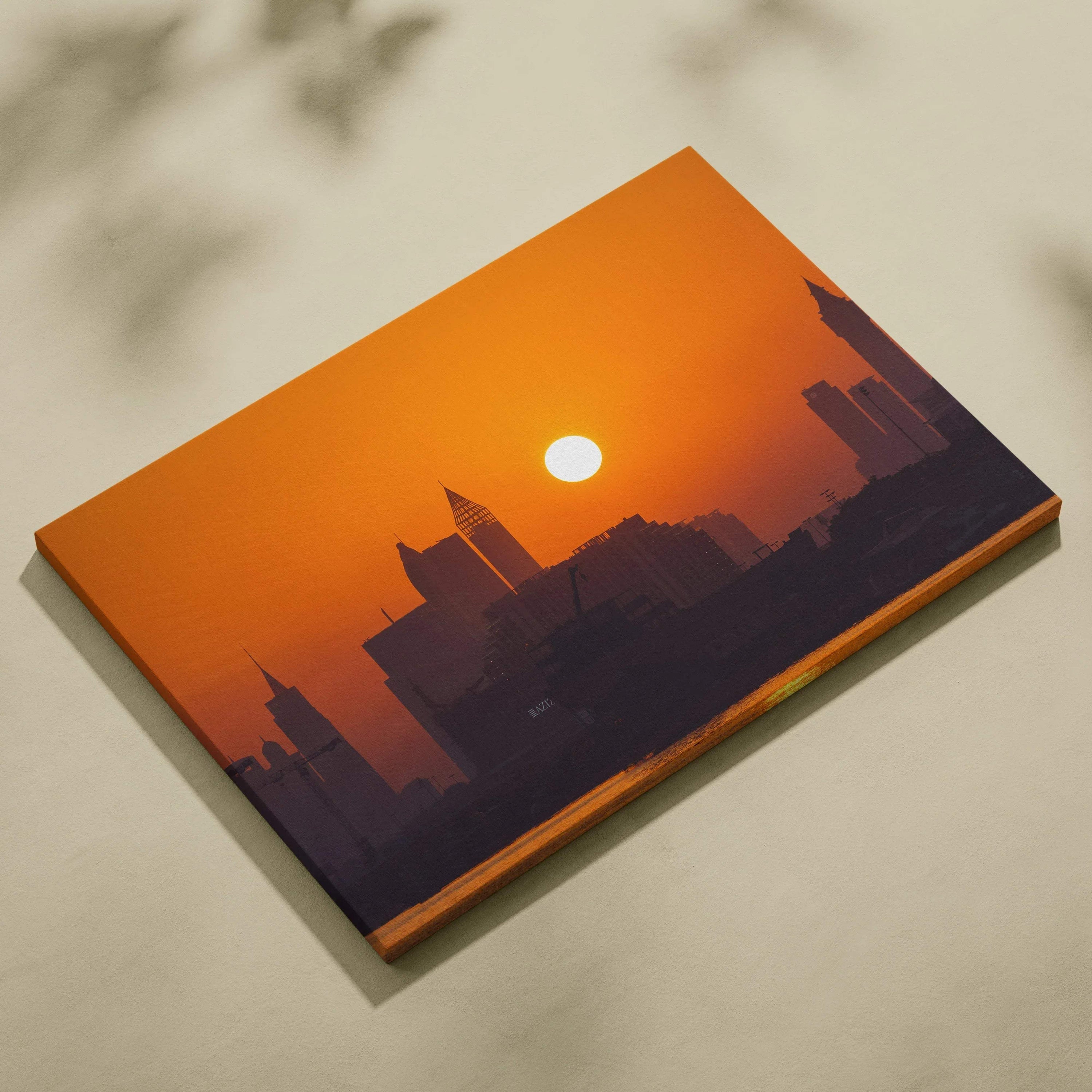 Canvas wall art featuring a dark city skyline silhouette against a vibrant orange sunset with the sun centered above.