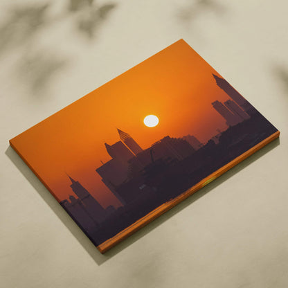 Canvas wall art featuring a dark city skyline silhouette against a vibrant orange sunset with the sun centered above.