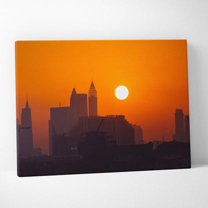 Canvas wall art featuring a city skyline silhouette at sunset with a vibrant orange sky and a bright sun.