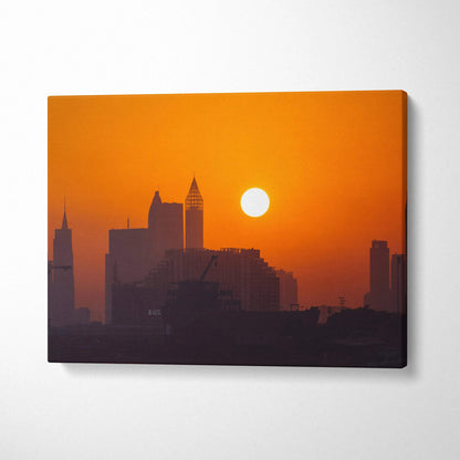 Sunset city skyline with glowing sun canvas wall art in warm orange tones.