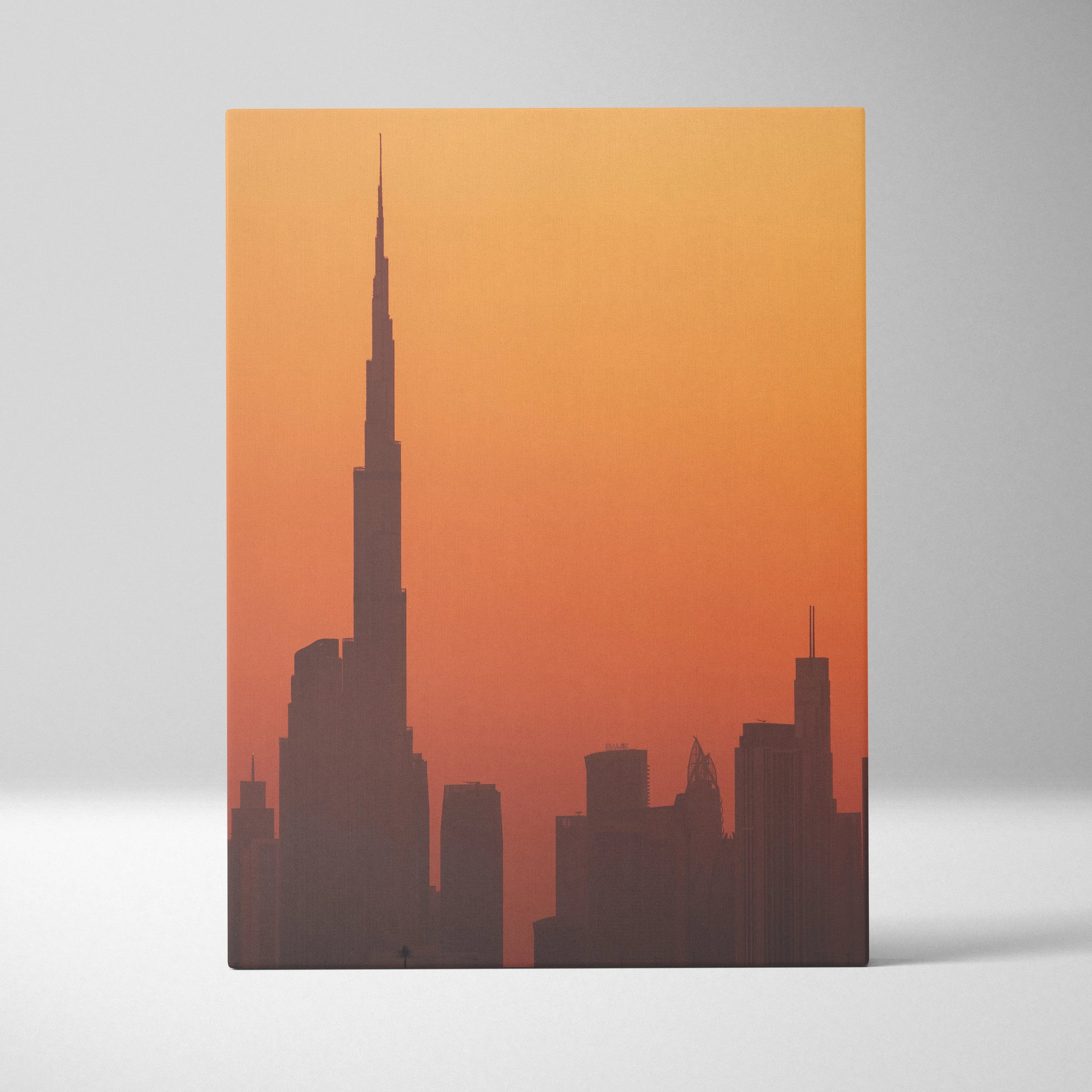 Canvas wall art featuring a silhouette of a city skyline with a tall, slender building against a warm orange gradient sky.