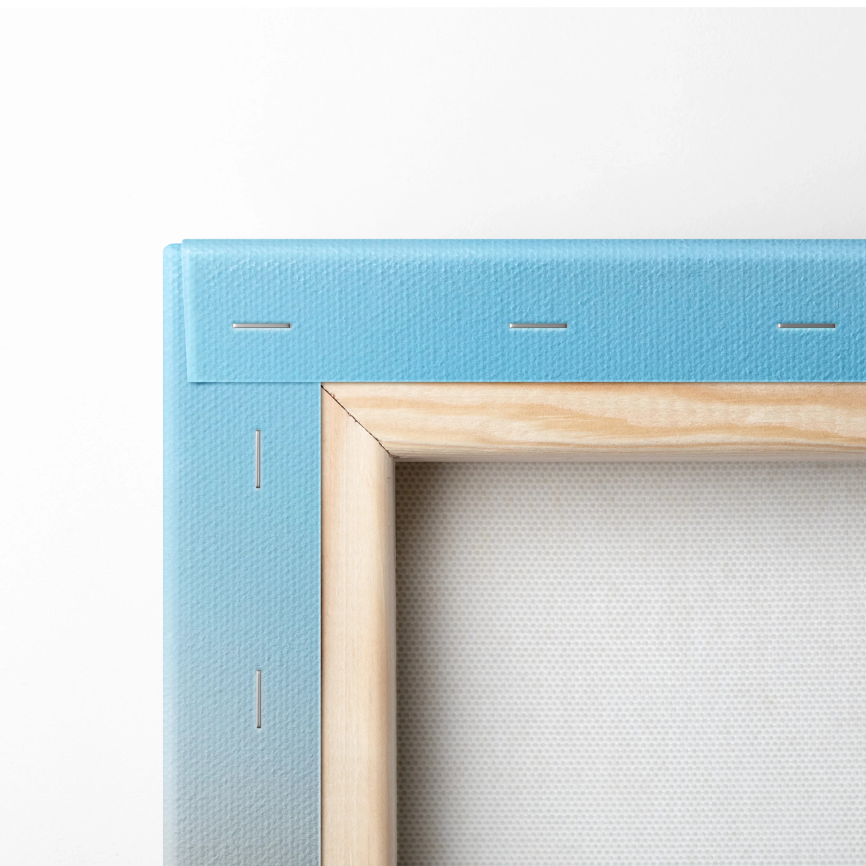 Close-up of stretched blue canvas fabric wrapped around wooden frame with metal staples detailing for wall art display.