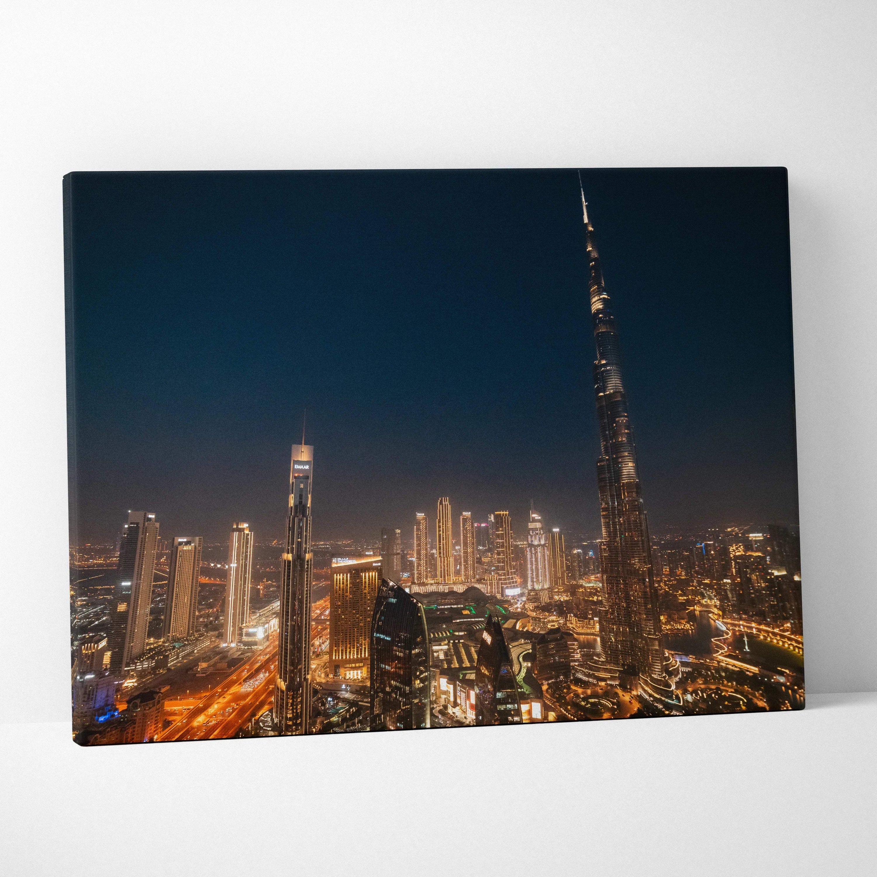 Canvas wall art featuring a nighttime cityscape with illuminated buildings and skyscrapers including a tall, slender tower.