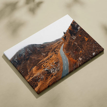 Canvas wall art featuring a winding road through vibrant autumn hills with rich orange and brown foliage.