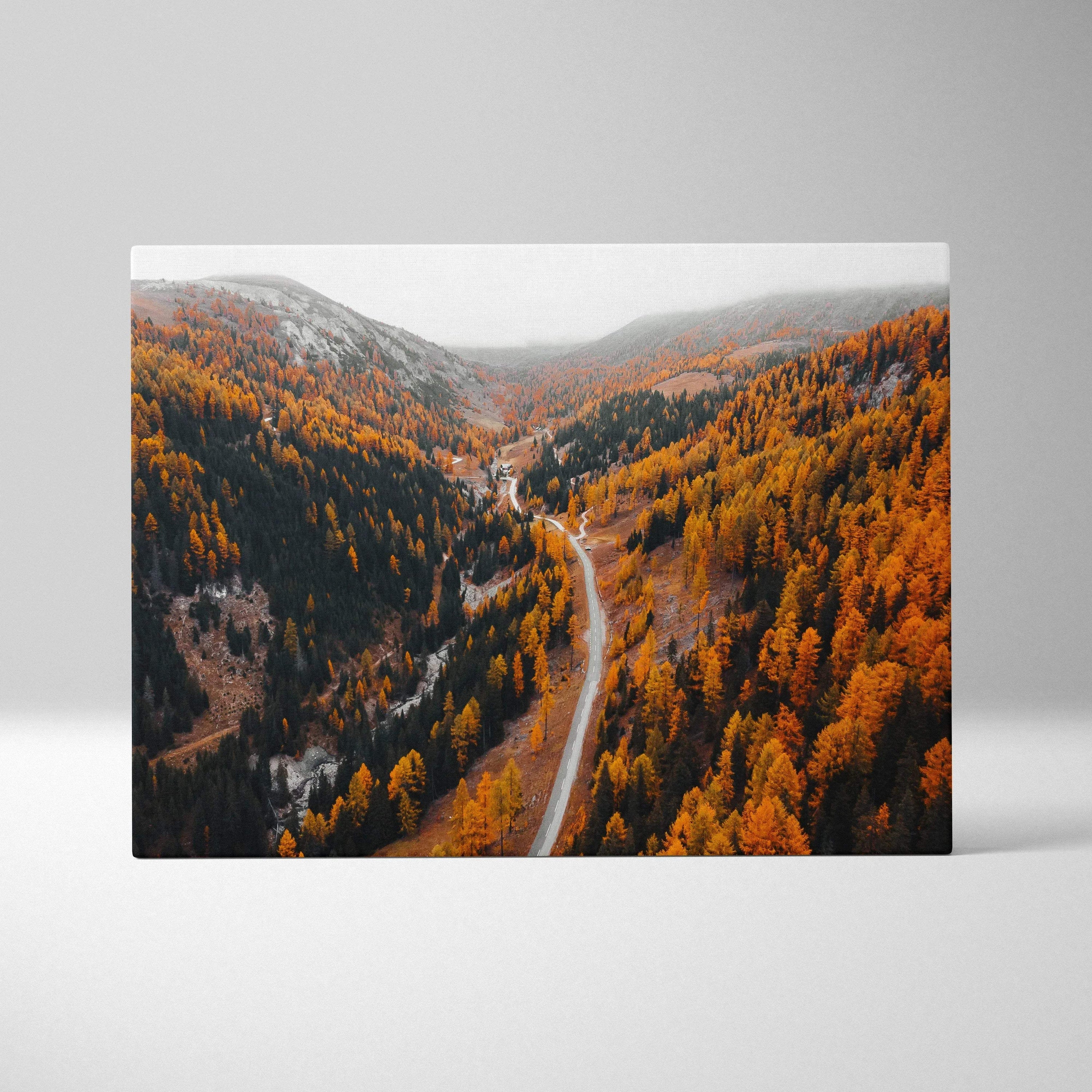Autumn canvas wall art featuring winding road through vibrant orange and yellow fall foliage under clear sky.