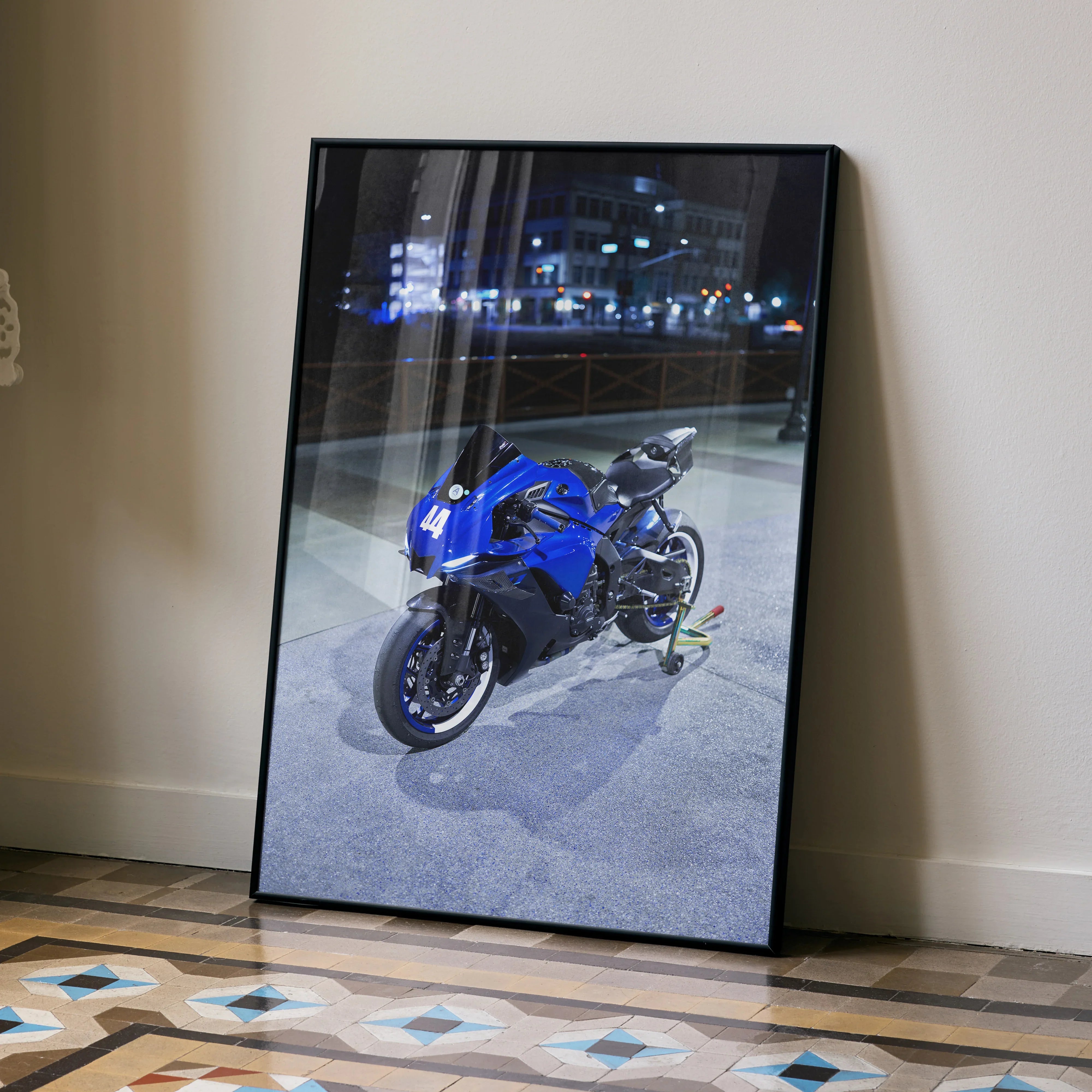 Yamaha R1 motorcycle poster in blue and black framed wall art leaning against white wall on tiled floor.