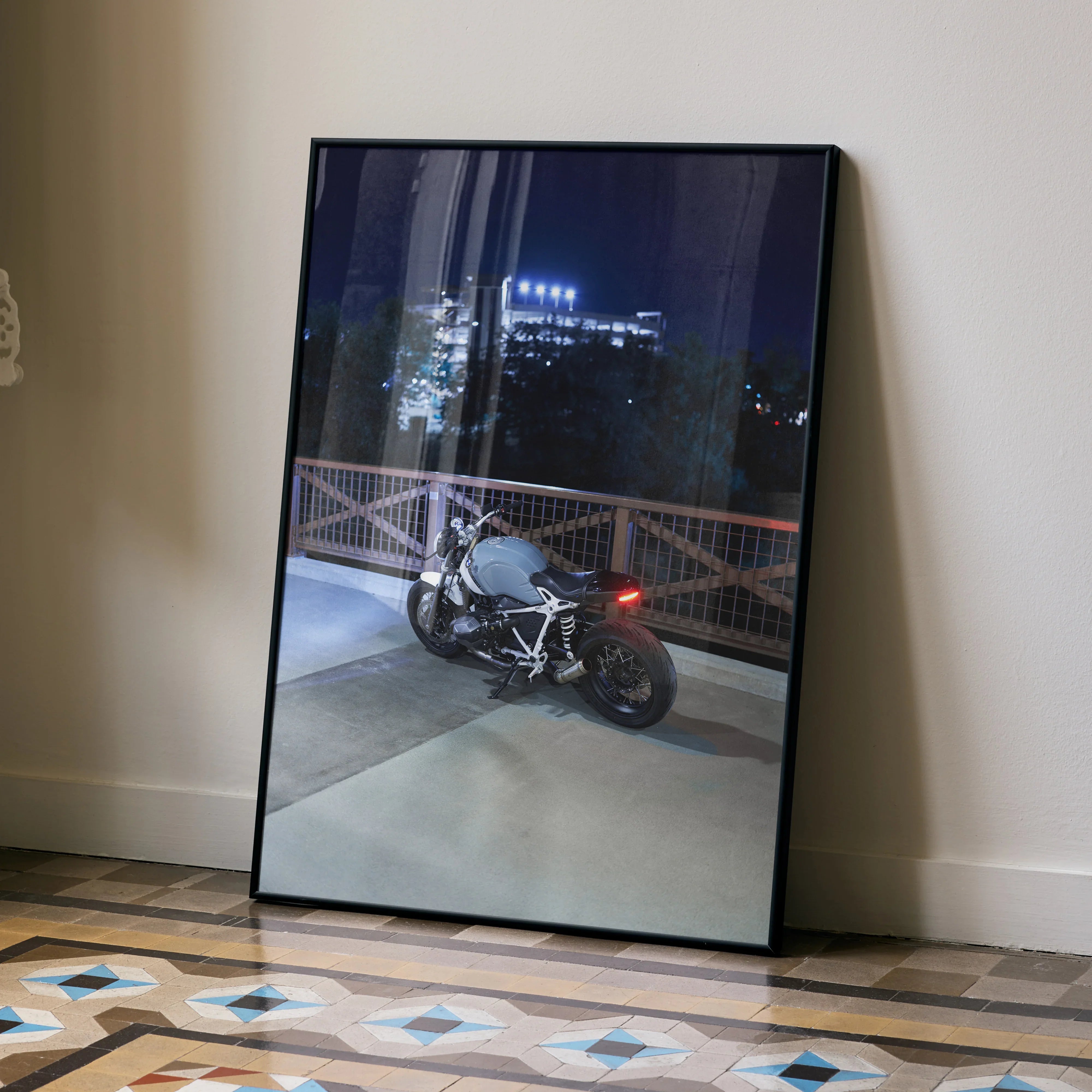 BMW R Nine T motorcycle at night on rooftop, framed poster wall art leaning on floor.