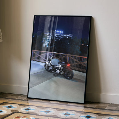 BMW R Nine T motorcycle at night on rooftop, framed poster wall art leaning on floor.