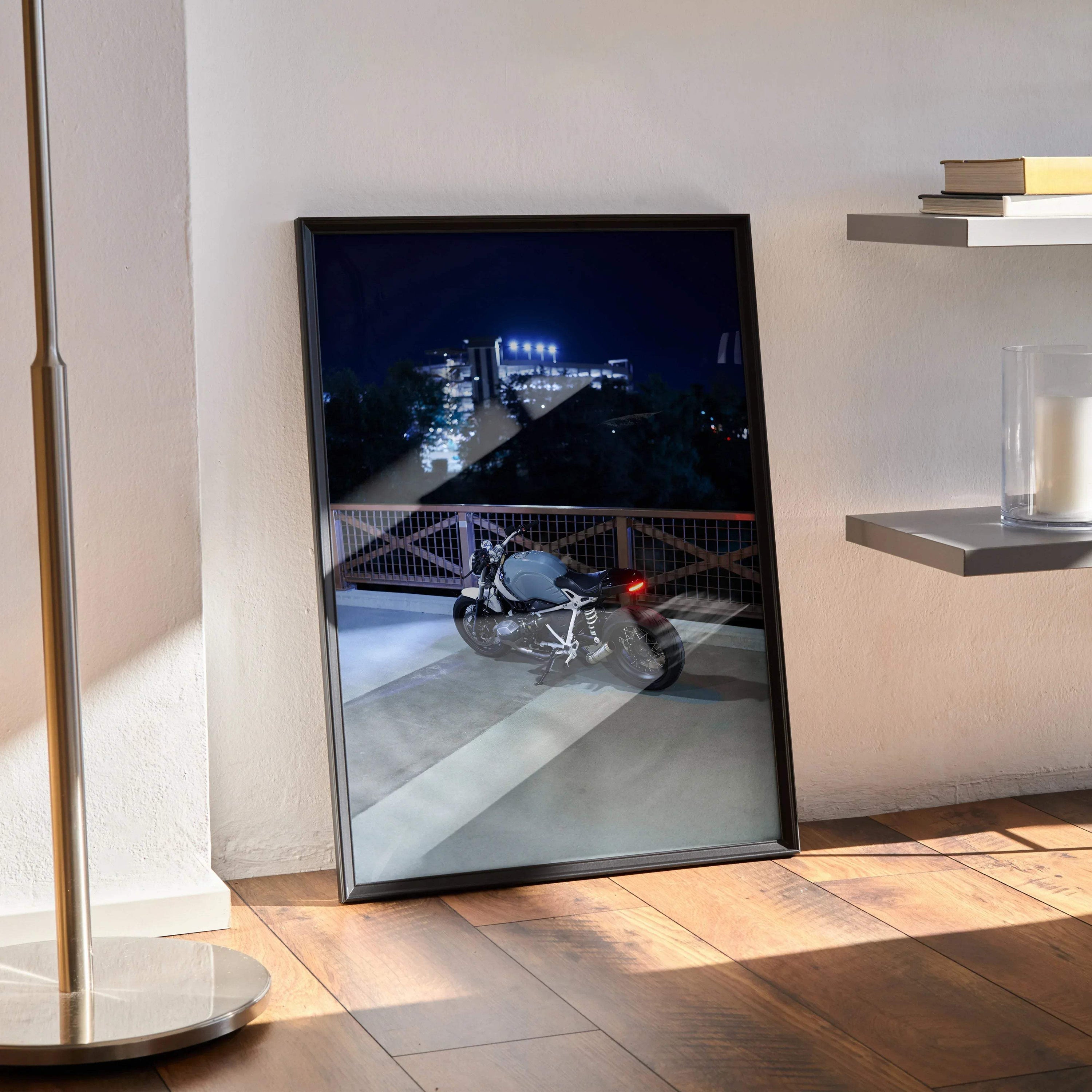 BMW R Nine T motorcycle poster with night cityscape, framed wall art leaning on floor.
