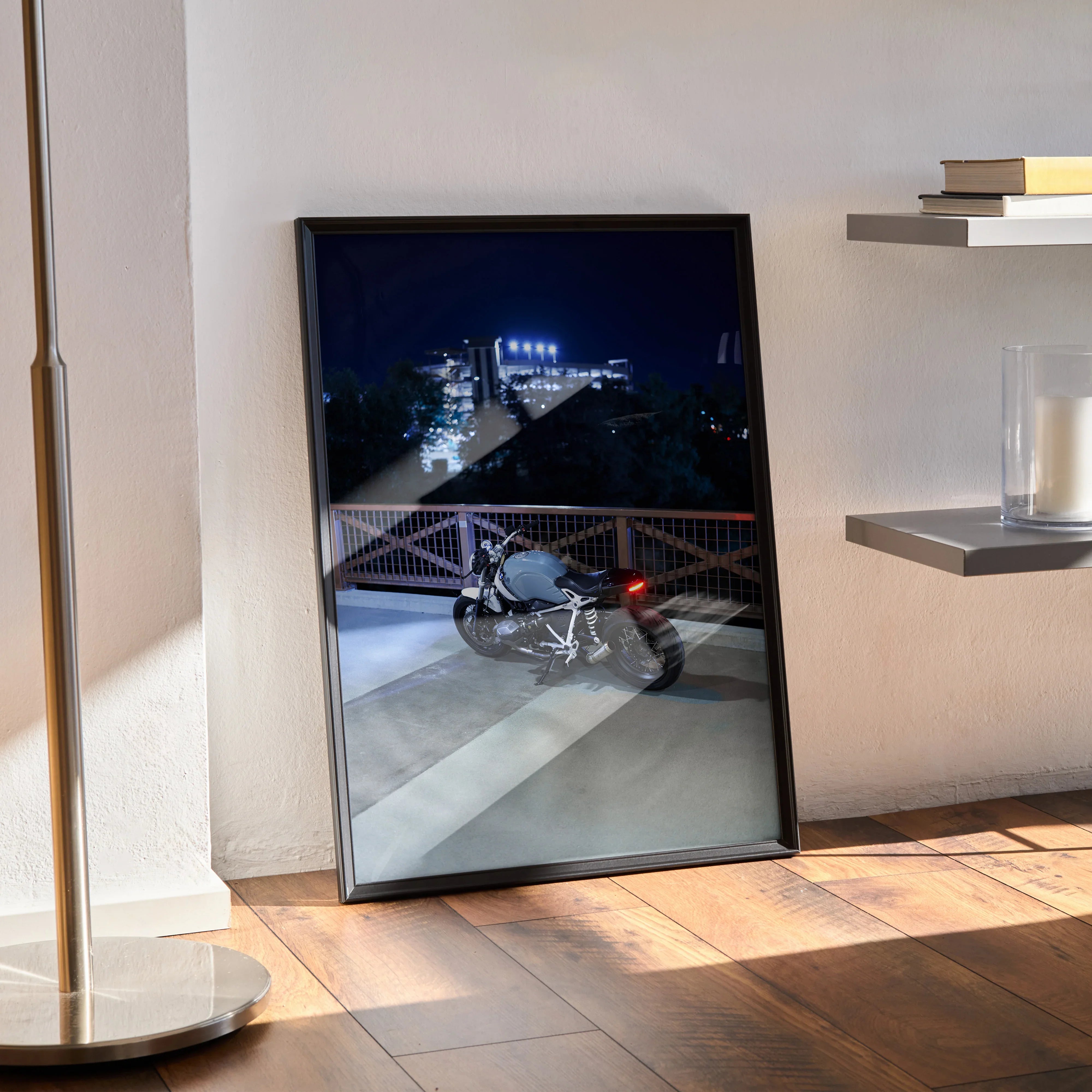 BMW R Nine T motorcycle poster with night cityscape, framed wall art leaning on floor.