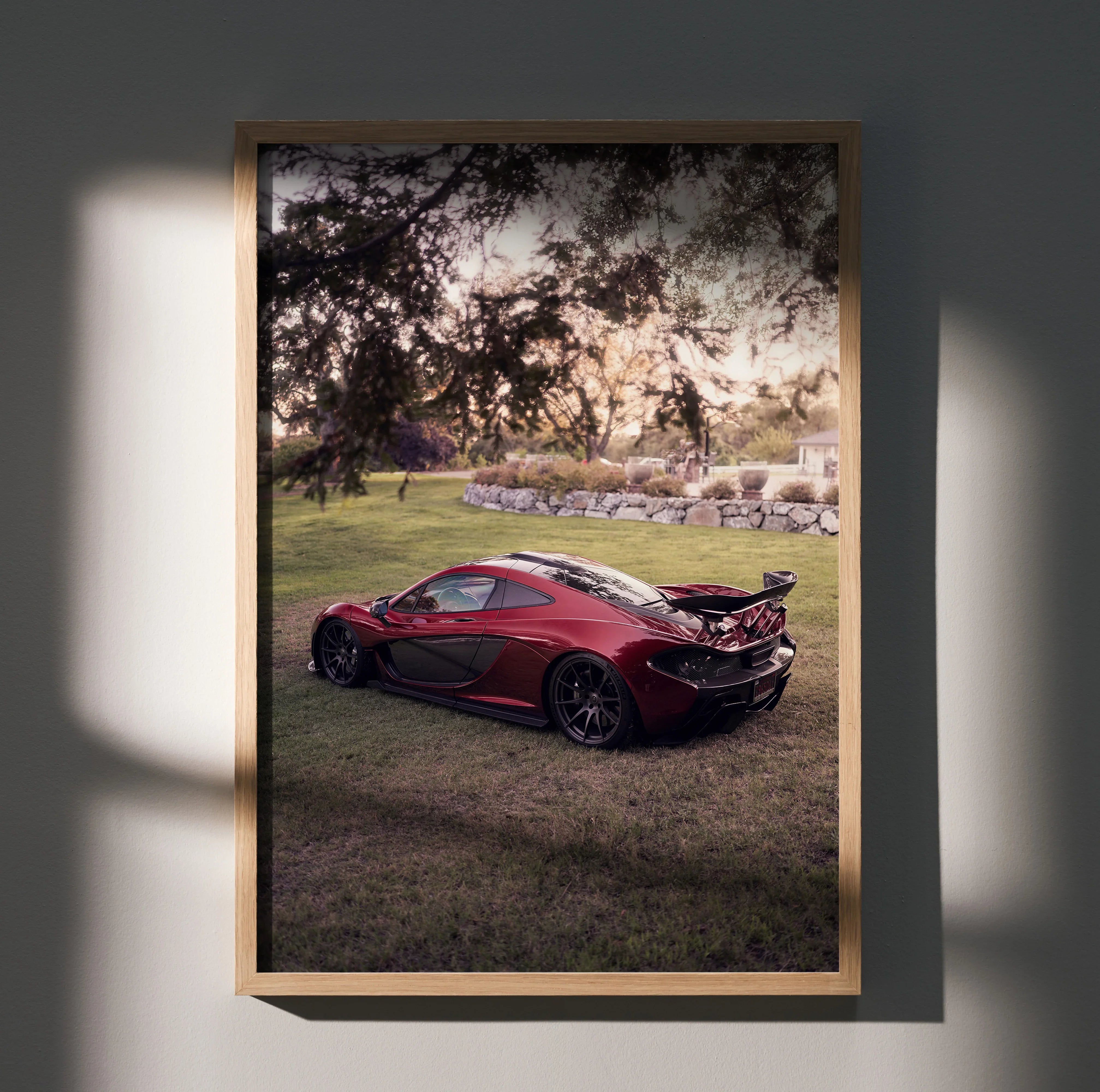 McLaren P1 poster wall art featuring red sports car parked on grass under tree at sunset.