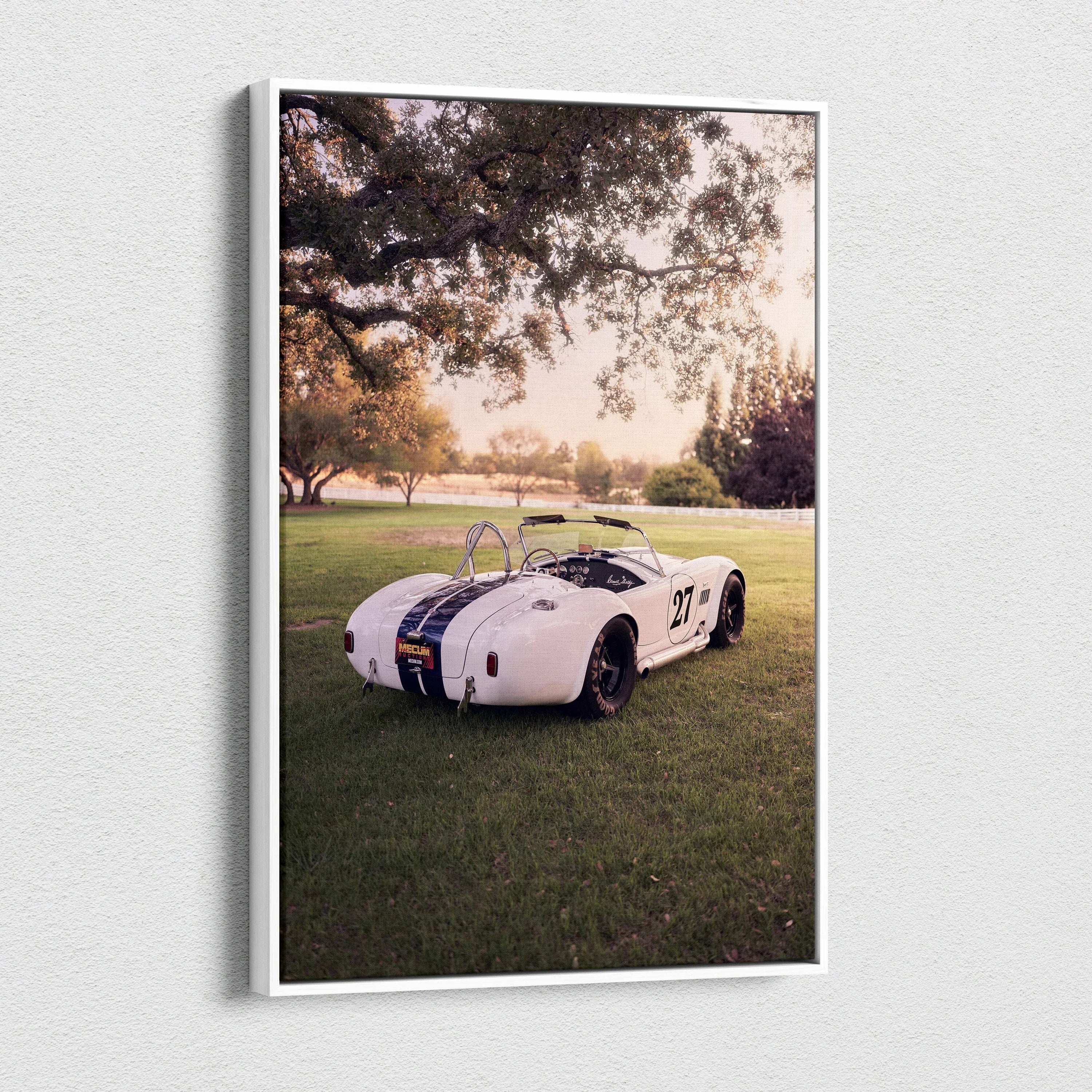 Vertical canvas wall art featuring a white Shelby Cobra parked on grass under large trees at sunset.