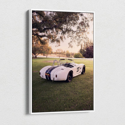 Vertical canvas wall art featuring a white Shelby Cobra parked on grass under large trees at sunset.