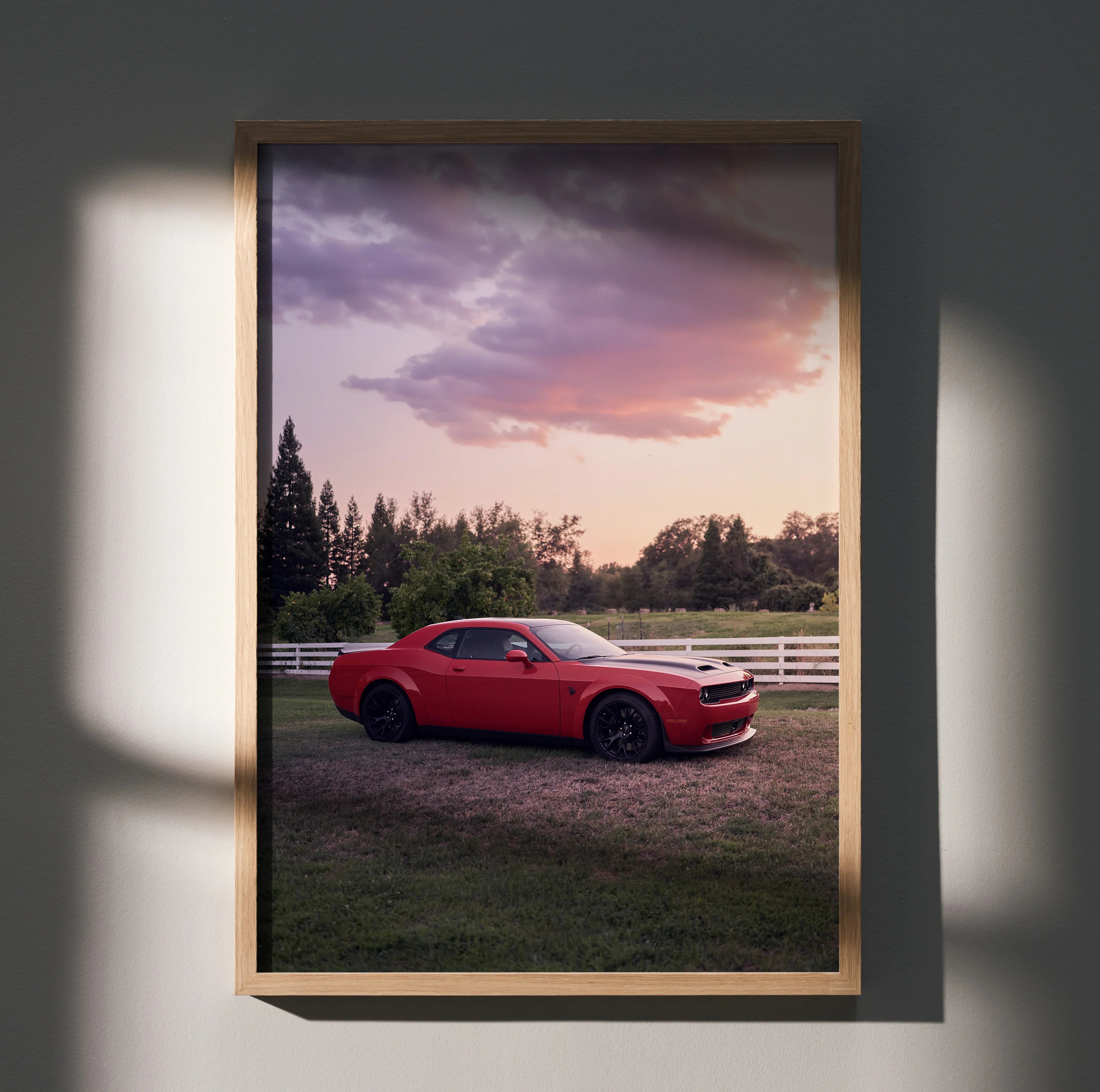 Red Dodge Challenger Hellcat parked on grass with sunset sky, framed poster wall art.