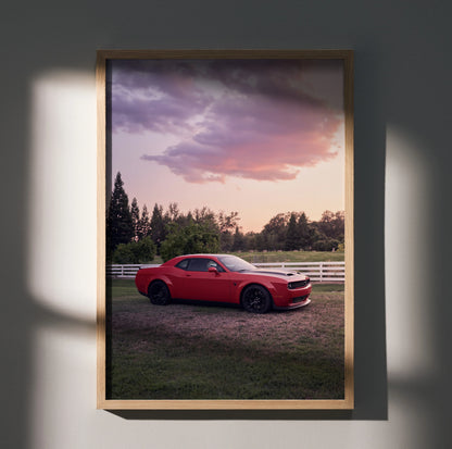 Red Dodge Challenger Hellcat parked on grass with sunset sky, framed poster wall art.
