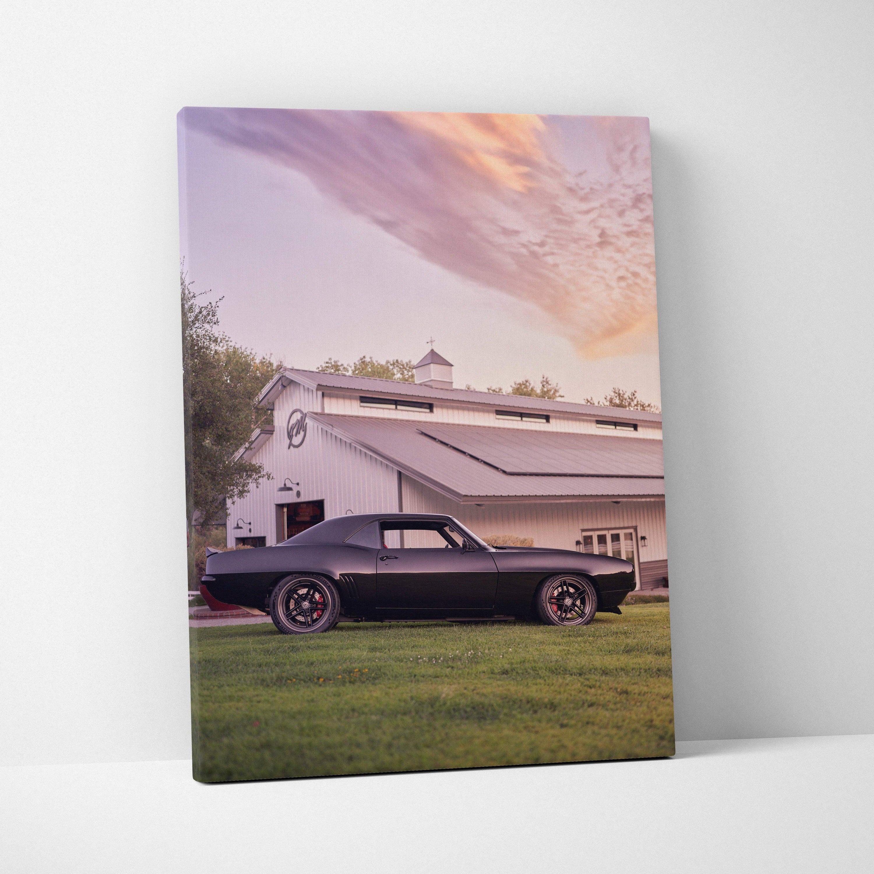 Canvas wall art featuring a black matte 1969 chevrolet camaro with red wheels against a rustic barn at sunset