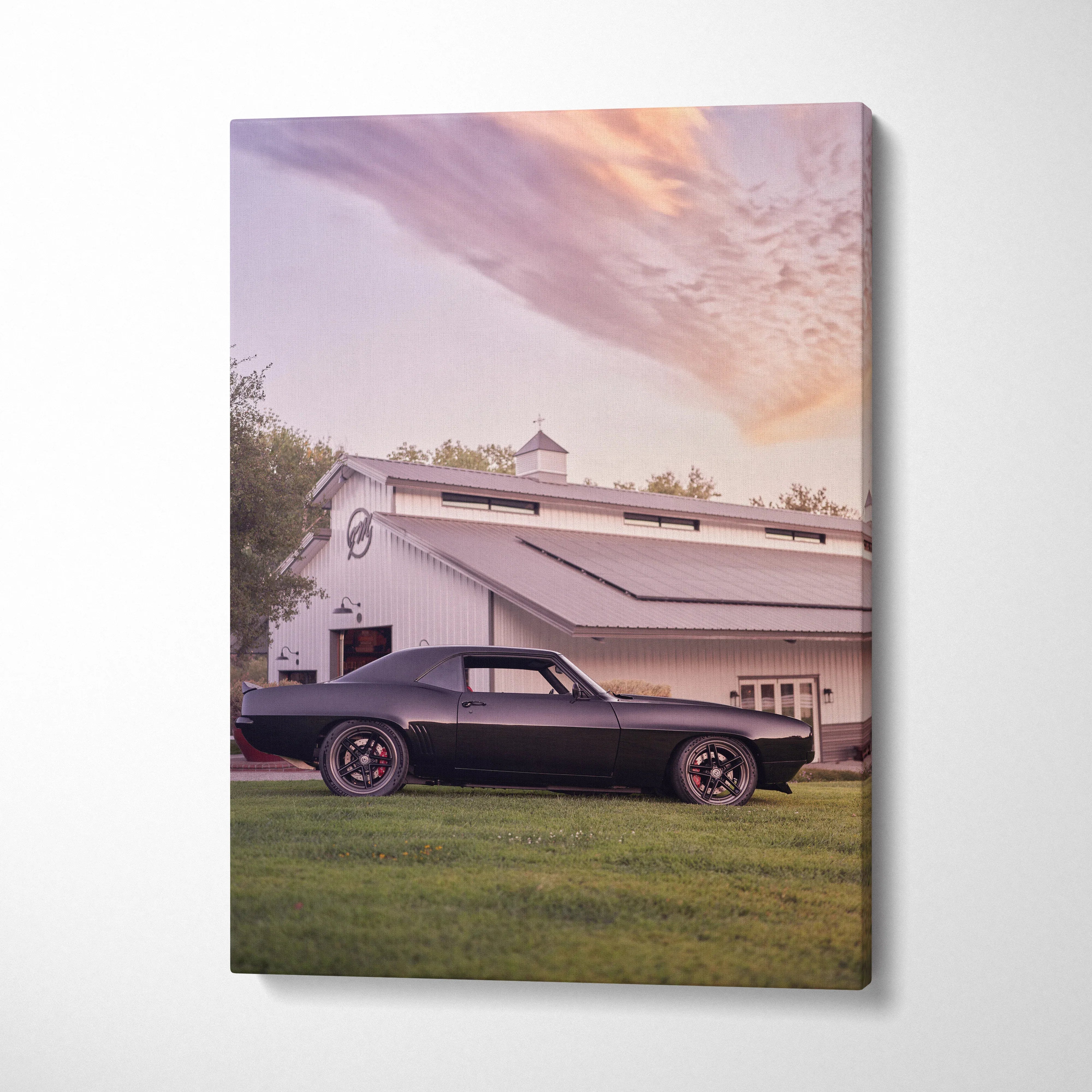 1969 black Camaro parked beside white barn under colorful sunset sky canvas wall art.