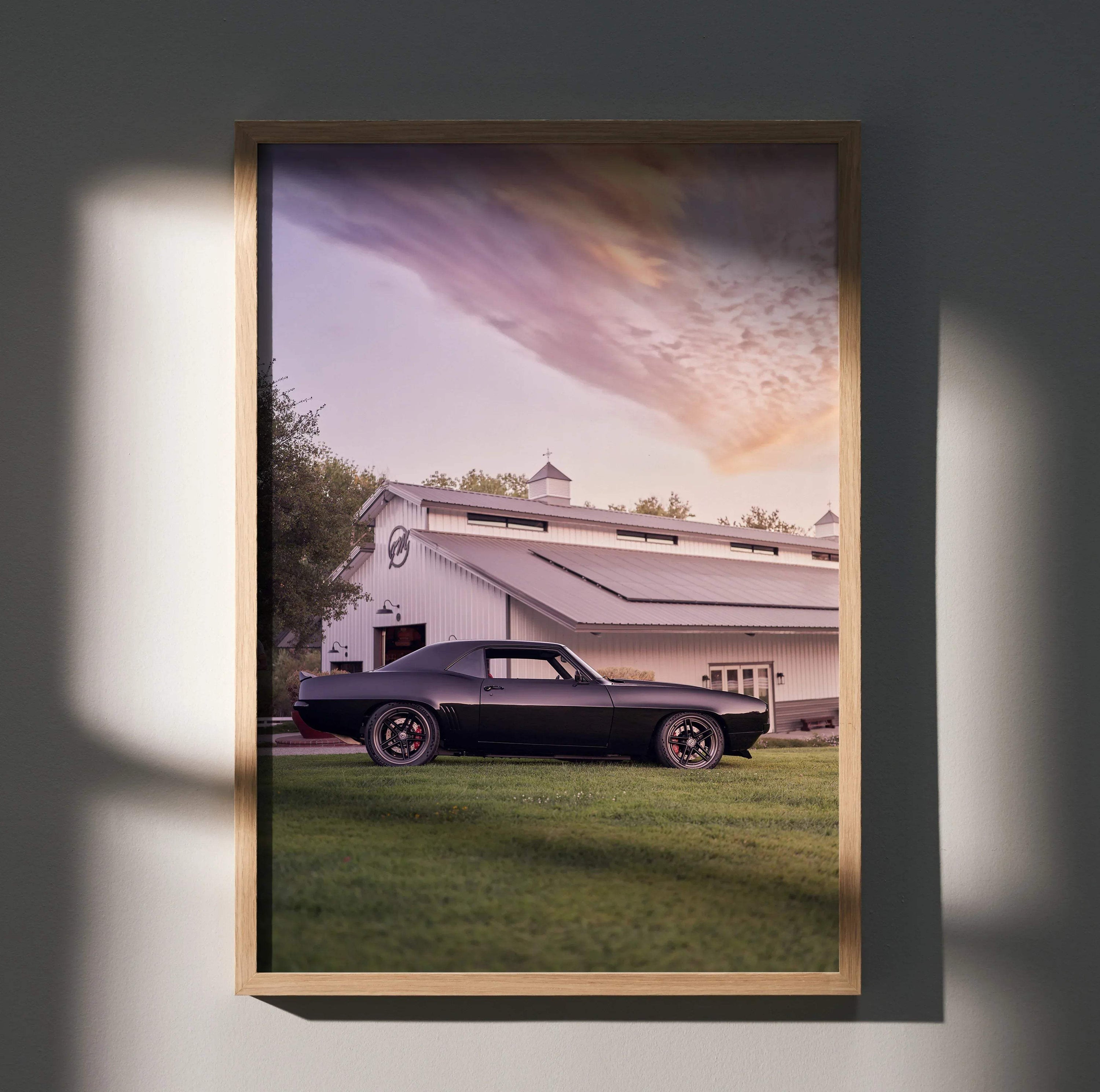 1969 black Camaro parked on grass in front of white barn under colorful sunset sky wall art poster.