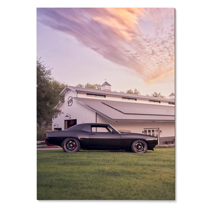 1969 black Camaro parked on grass in front of white barn at sunset poster wall art.