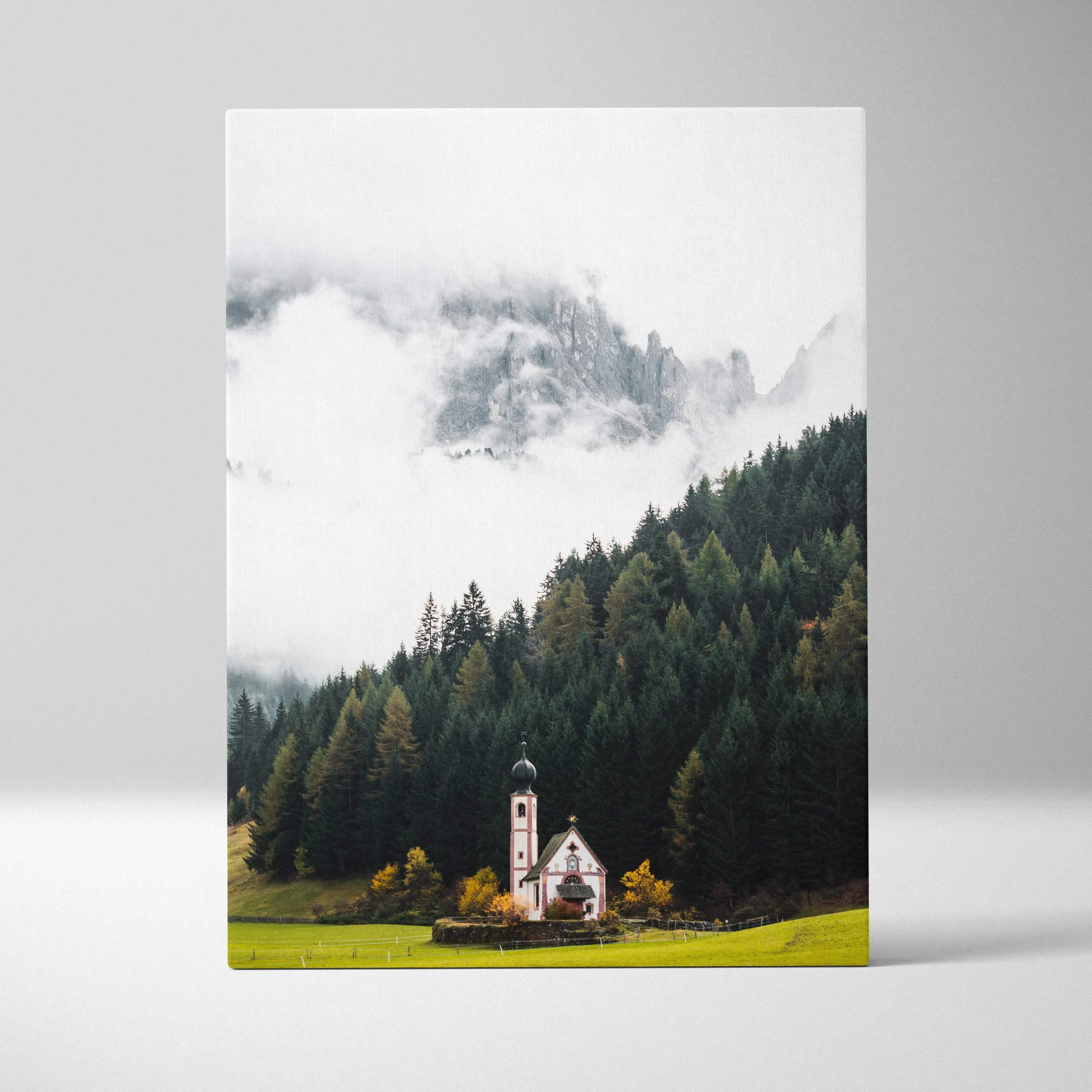 Vertical canvas art wall print featuring a small church amid green trees and misty mountains.