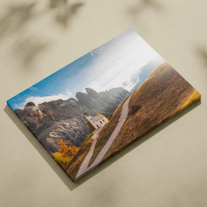 Canvas wall art featuring modern architecture with rugged mountains, a winding path, and a small building under a blue sky.