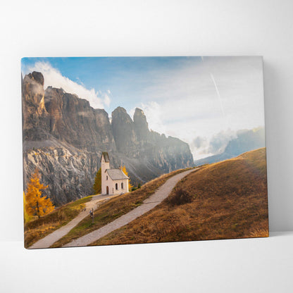 Canvas art print featuring a small white church on a winding path with rugged mountain cliffs and autumn foliage under a.