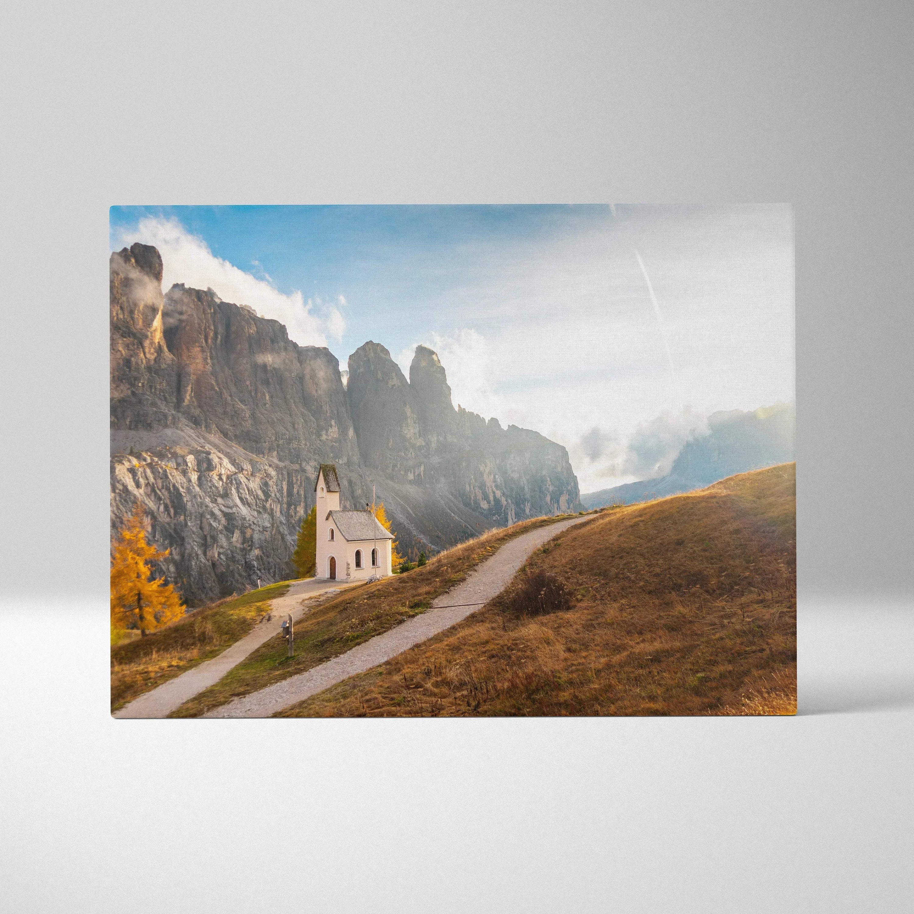 Canvas art print featuring a small white chapel on a winding path with rugged rocky cliffs and blue sky background.