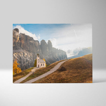 Canvas art print featuring a small white chapel on a winding path with rugged rocky cliffs and blue sky background.