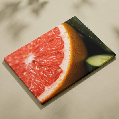 Canvas wall art featuring a close-up of a vibrant pink grapefruit slice with green leaves on a light background.
