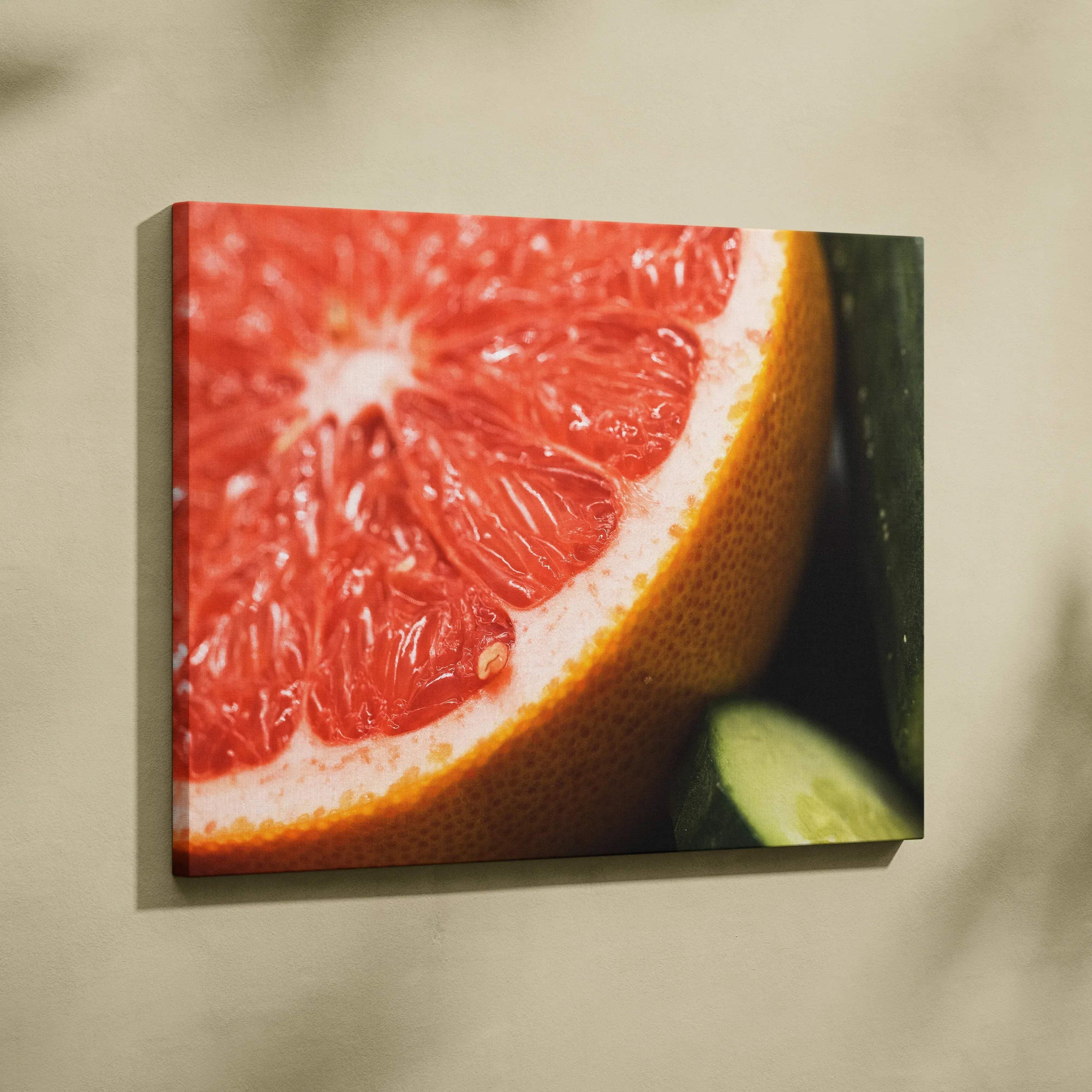 Canvas wall art featuring a close-up of a juicy red grapefruit slice with a cucumber on a neutral background.